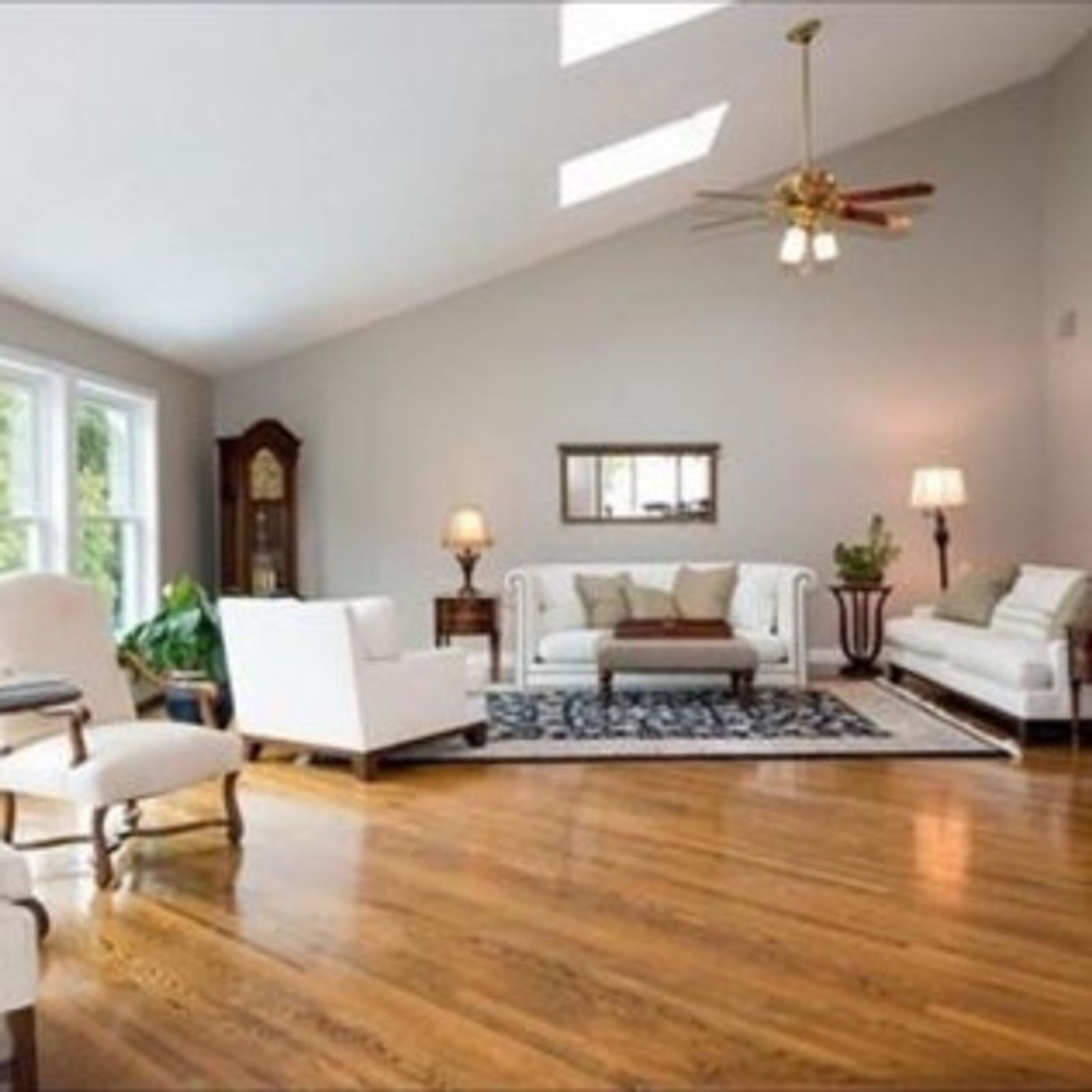 Spacious living room with hardwood floors, white furniture, and a grandfather clock.