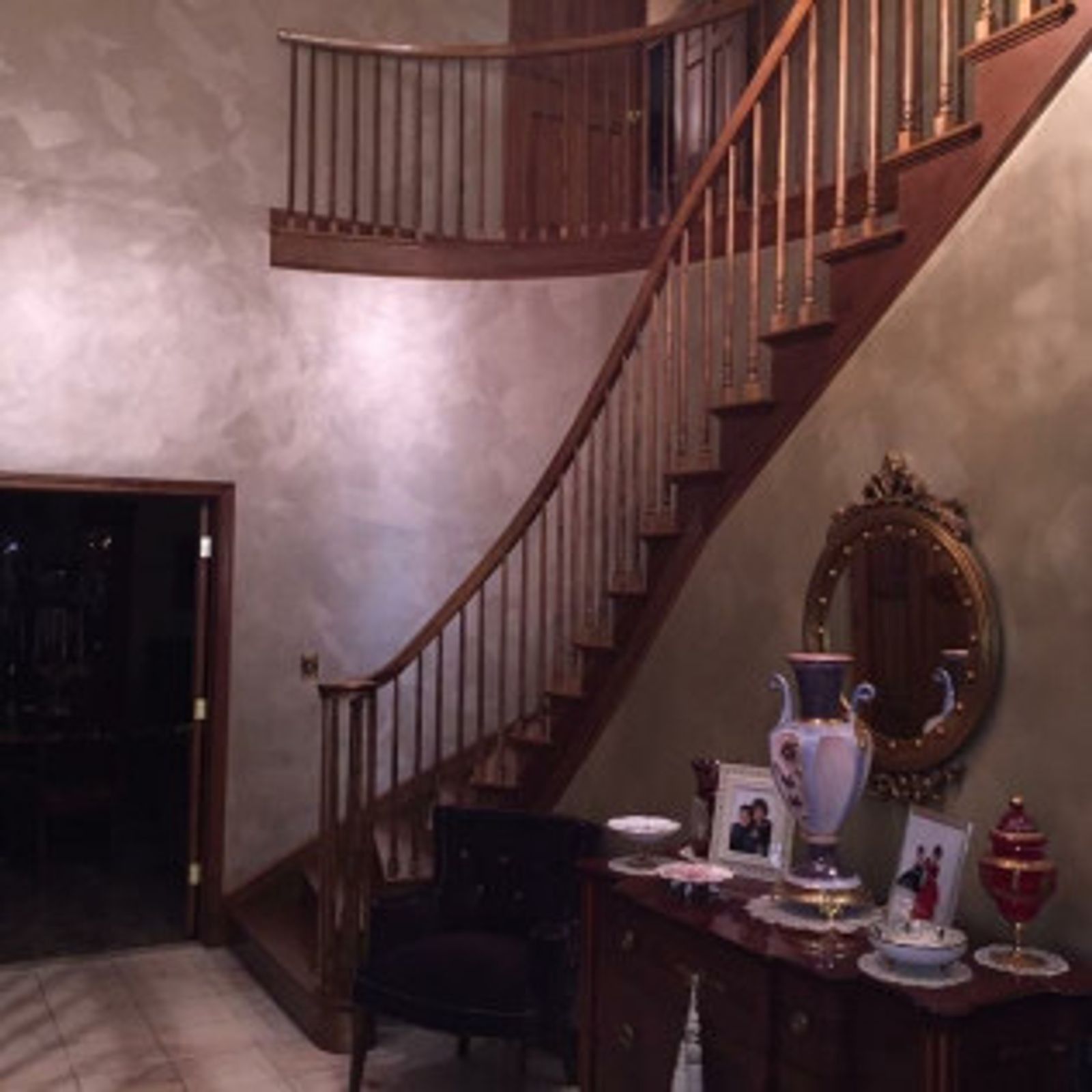 Wooden staircase with ornate railing and curved design, decorated with furniture and framed photos.