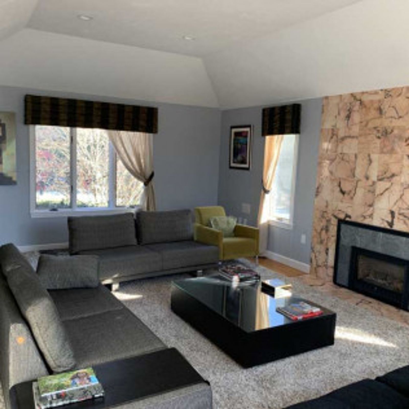 Living room with grey sectional sofa, fireplace, and large windows with curtains.