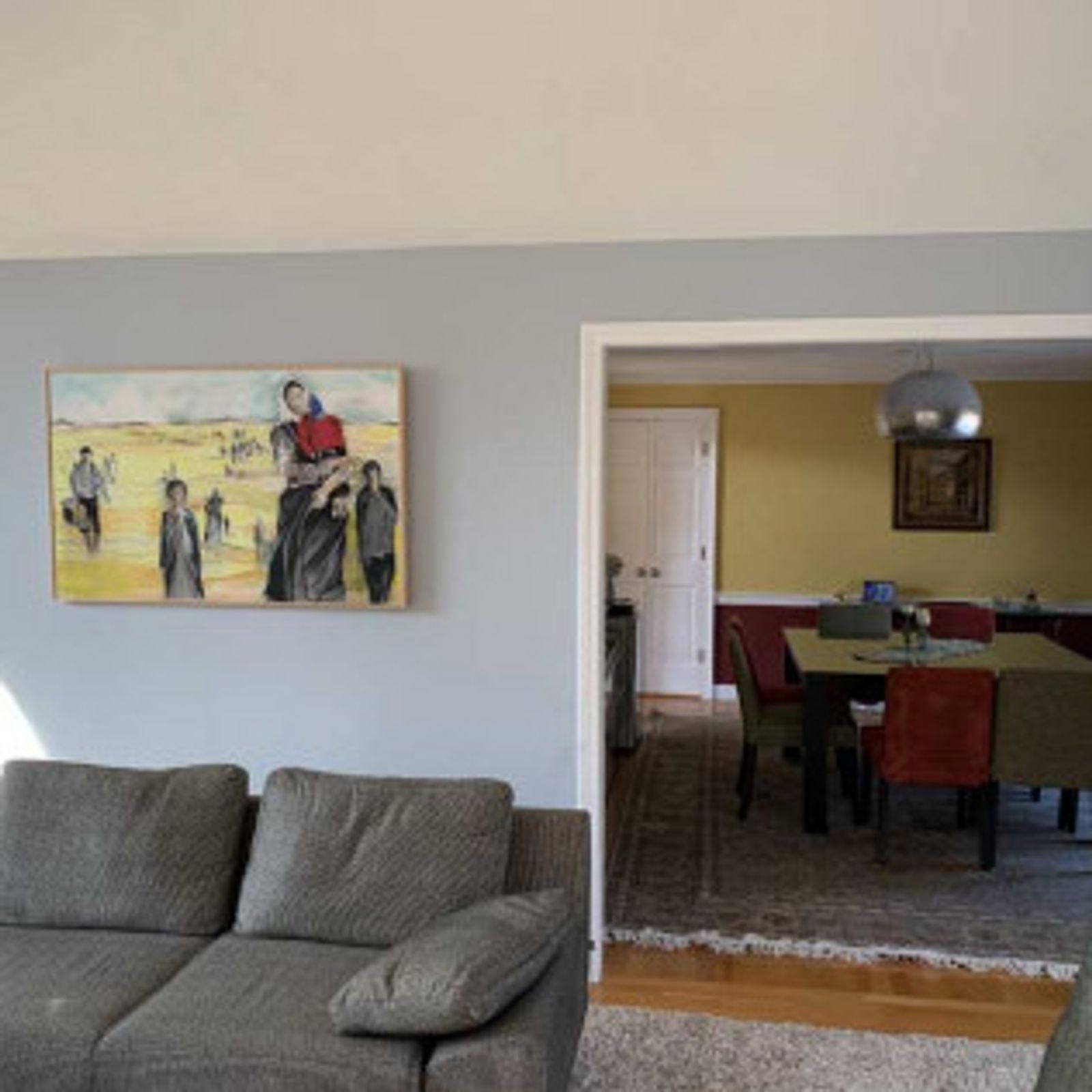 Living room with gray walls, sofa, painting, and view of dining room.