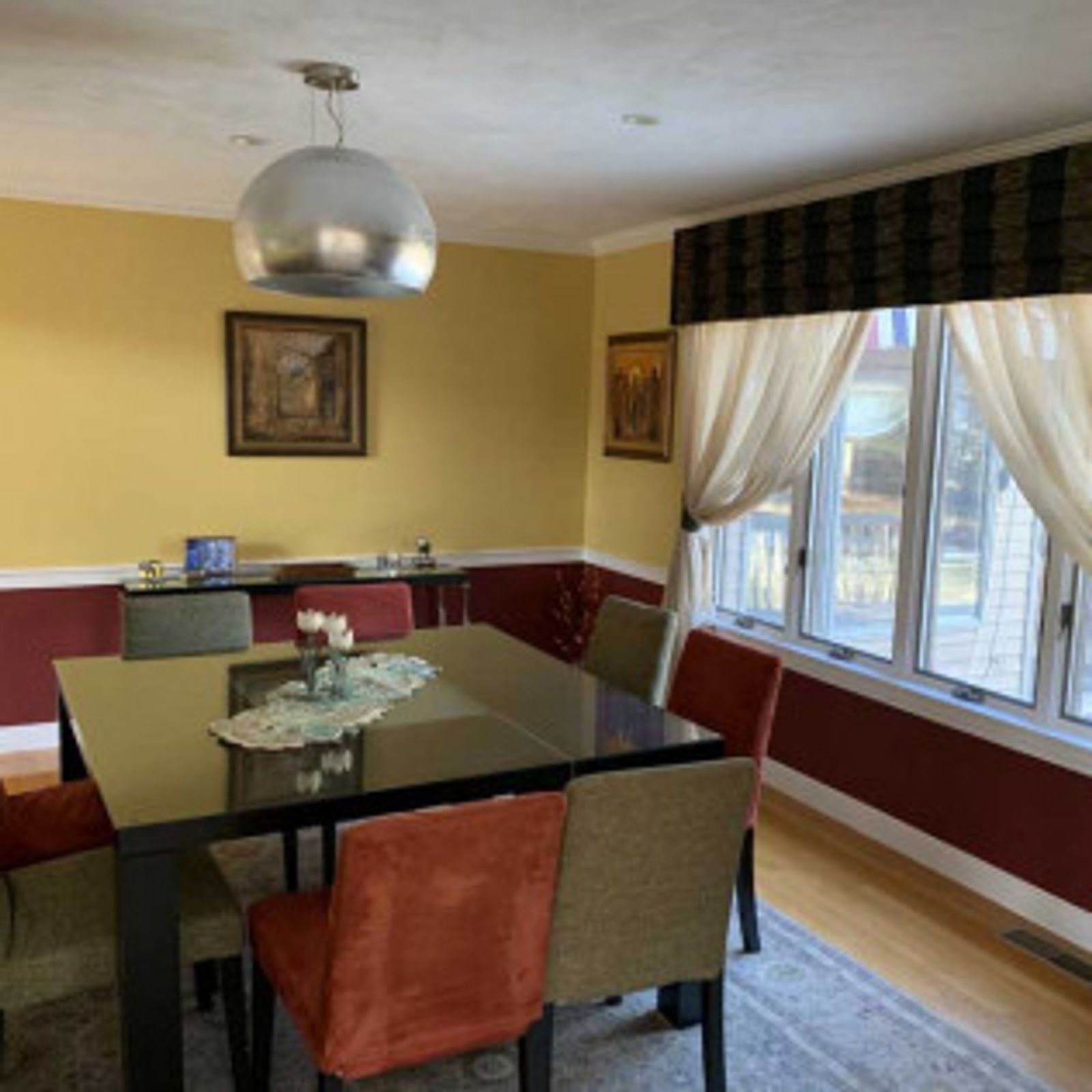 Dining room with a black table, colorful chairs, and a large window with cream curtains.
