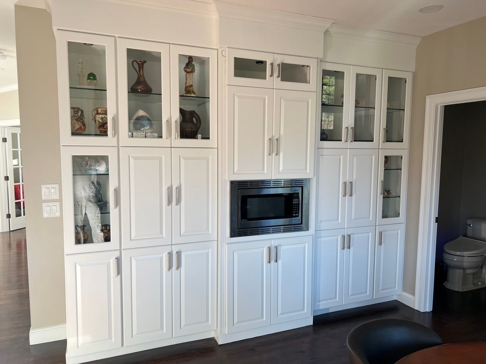 White kitchen cabinets with glass doors, microwave, and decorative items.