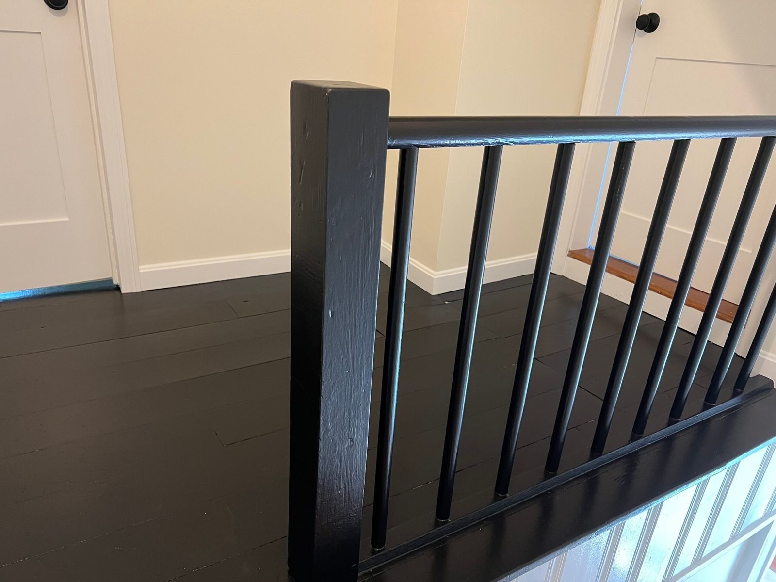 Black stair railing with vertical spindles, contrasting against a dark floor and beige walls.