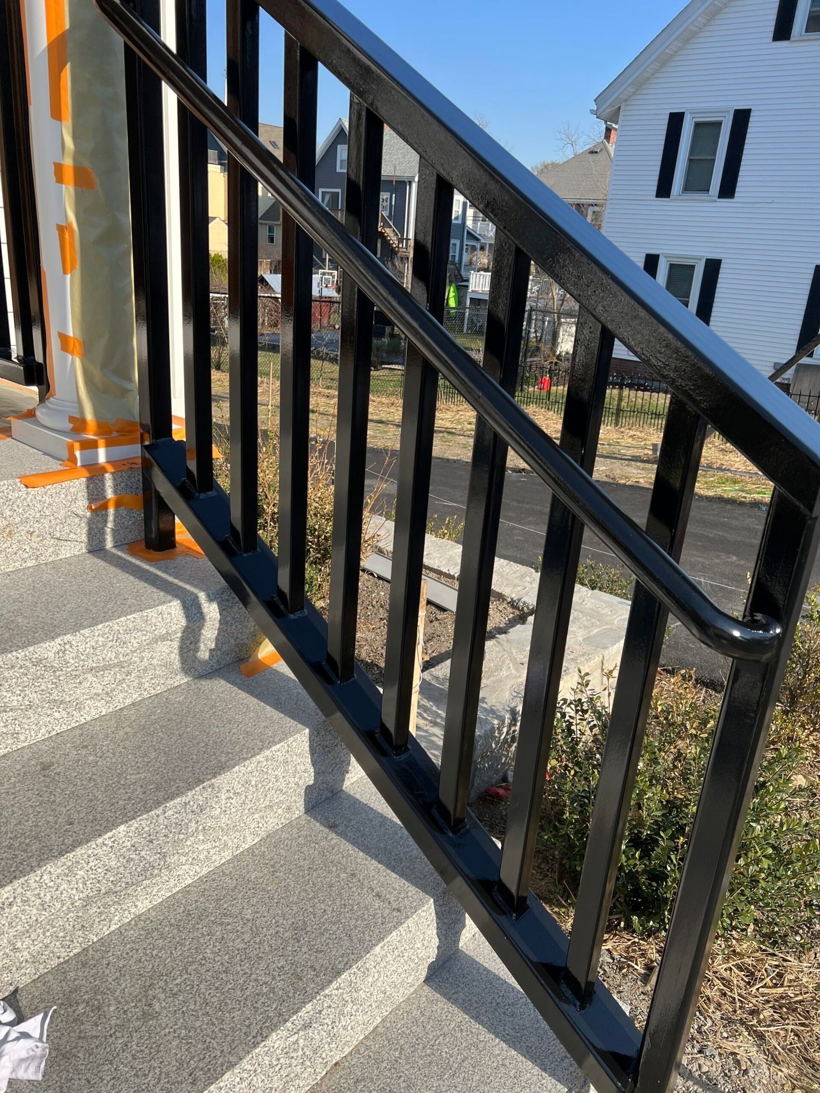 Black metal handrail on outdoor steps. Gray speckled concrete steps, white house in background.