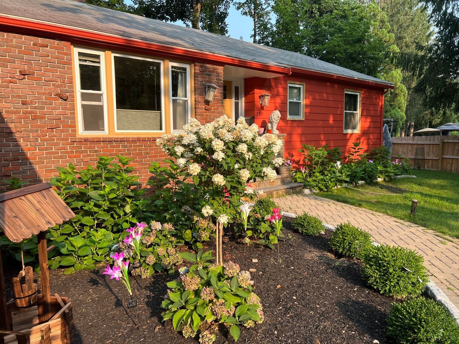 Red brick house with a well and flower garden, paved walkway.