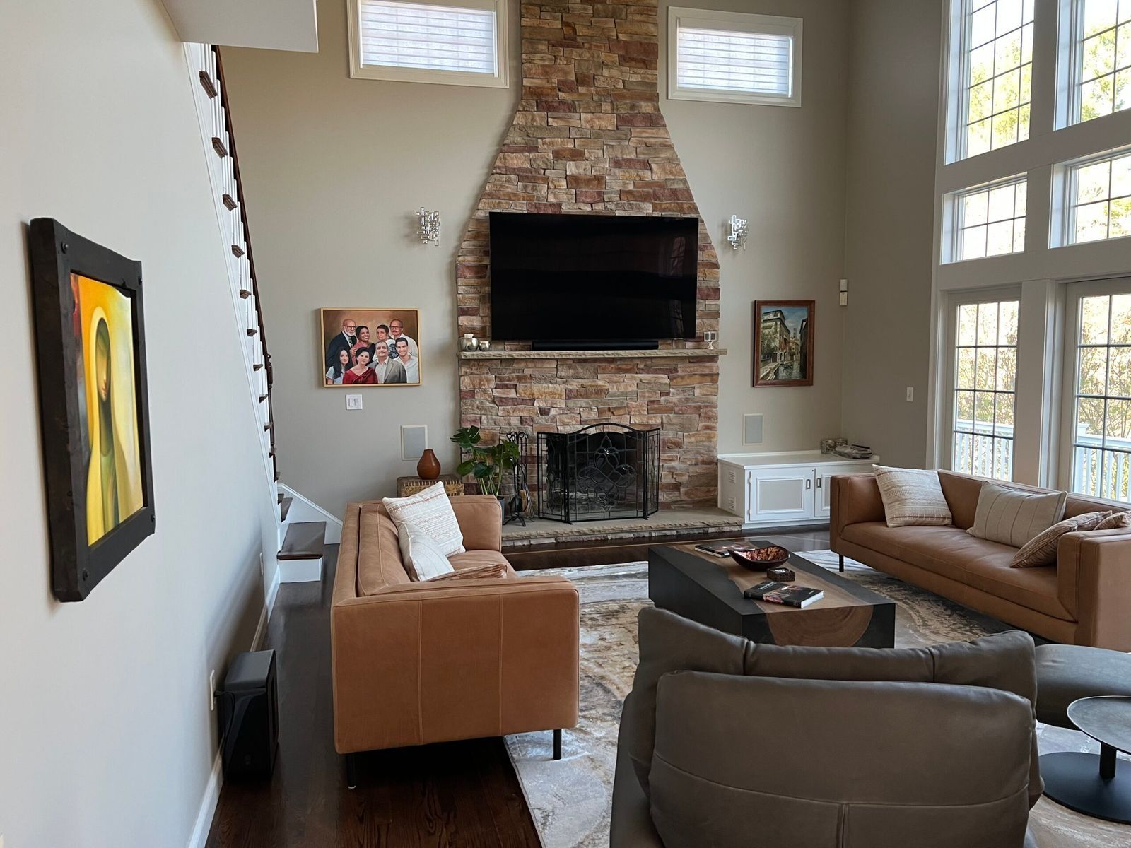 Living room with fireplace, TV, leather sofas, area rug, and artwork. Natural light from tall windows.