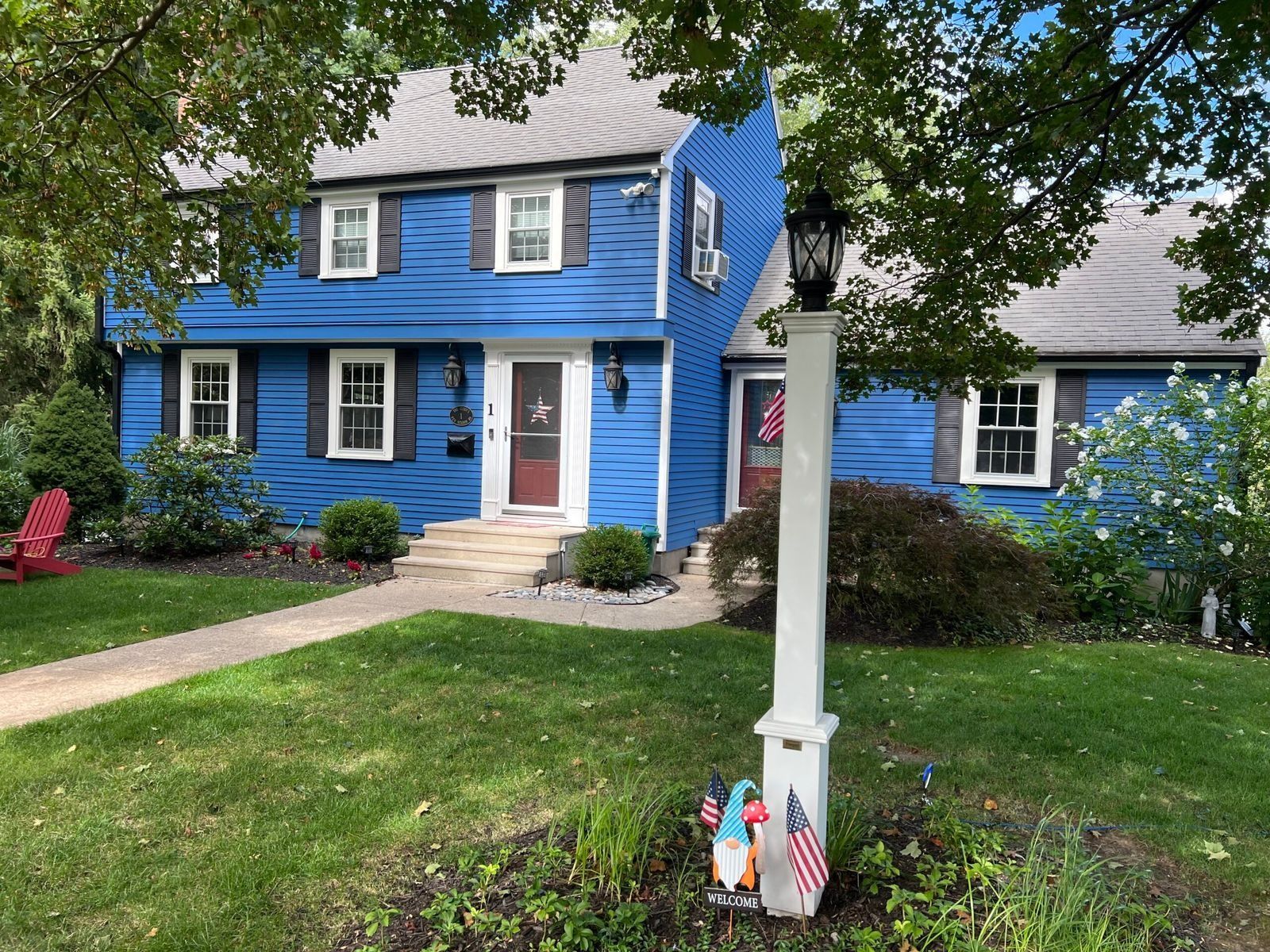 Blue two-story house with black shutters, a red door, and a white lamp post in front.