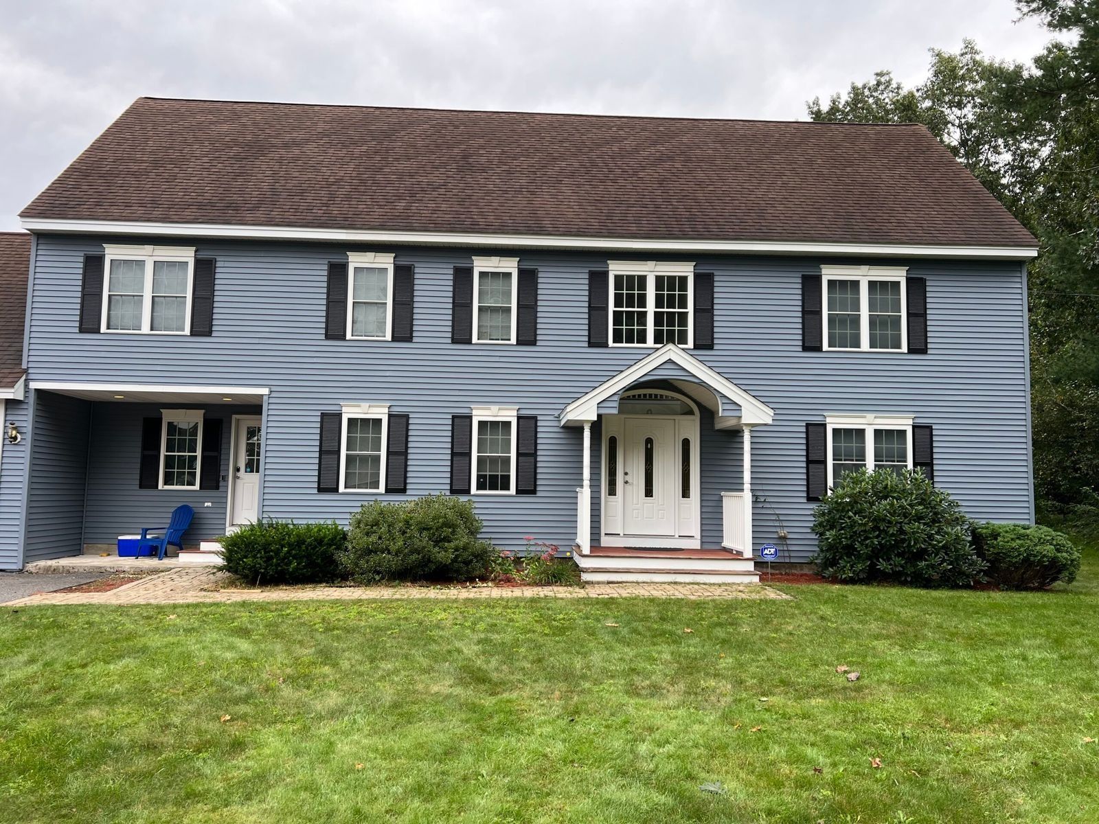 Two-story blue house with black shutters, white door, and wavy brown roof, set on green lawn.