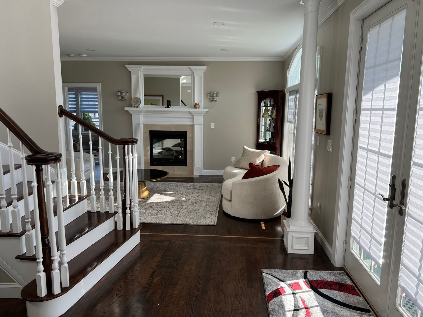 Entryway with stairs, fireplace, and arched white door with blinds. Dark wood floor and light-colored walls.