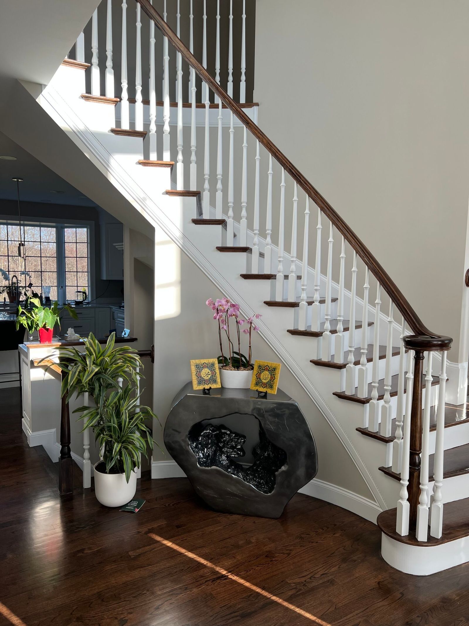 Staircase with white railing and brown steps. Dark wood floor. Large stone with amethyst interior serves as an entry table.