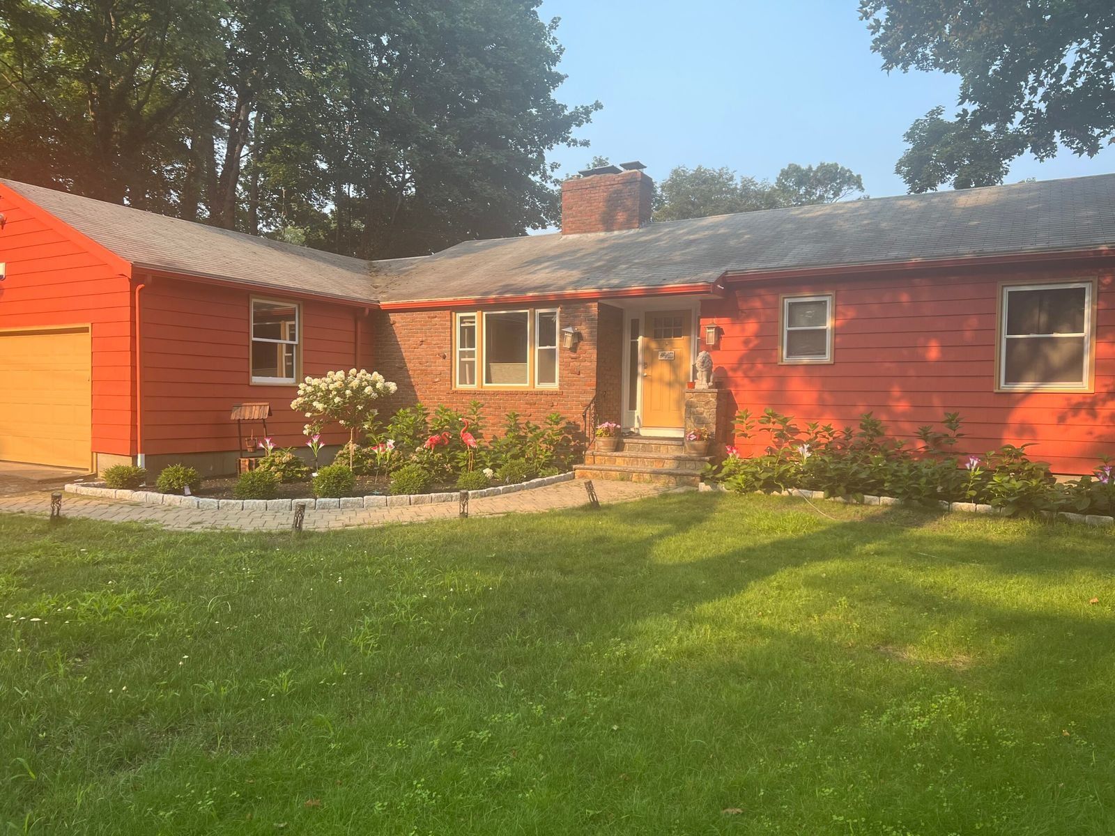 Red-painted house with a brick facade and a flower bed in front of green lawn.