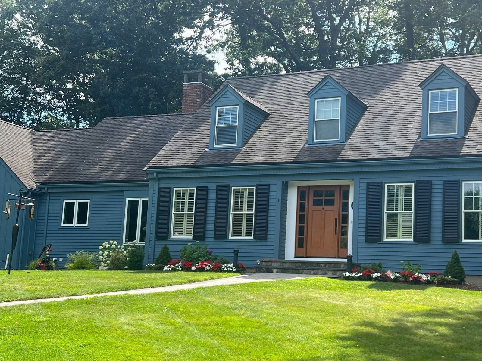 Blue house with dark roof, shutters, orange door, and well-kept lawn.