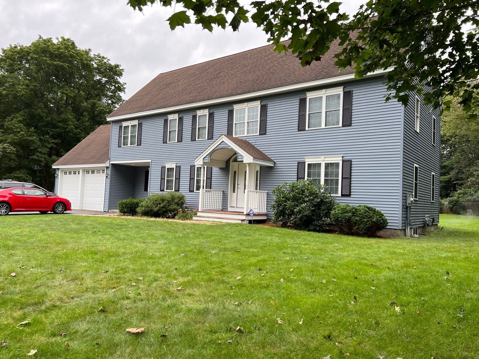 Two-story blue house with brown roof and garage. Red car parked in driveway, green lawn.