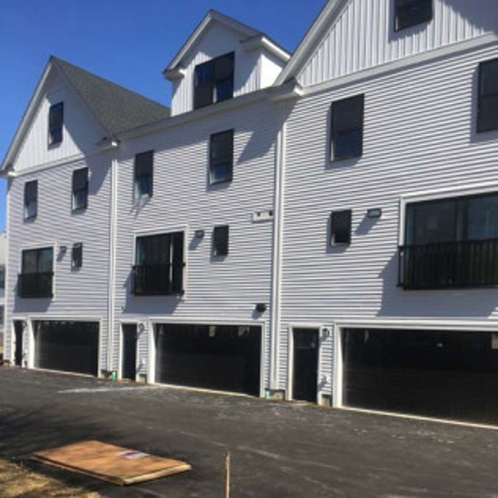Row of white townhouses with black garages, windows, and trim on a sunny day.