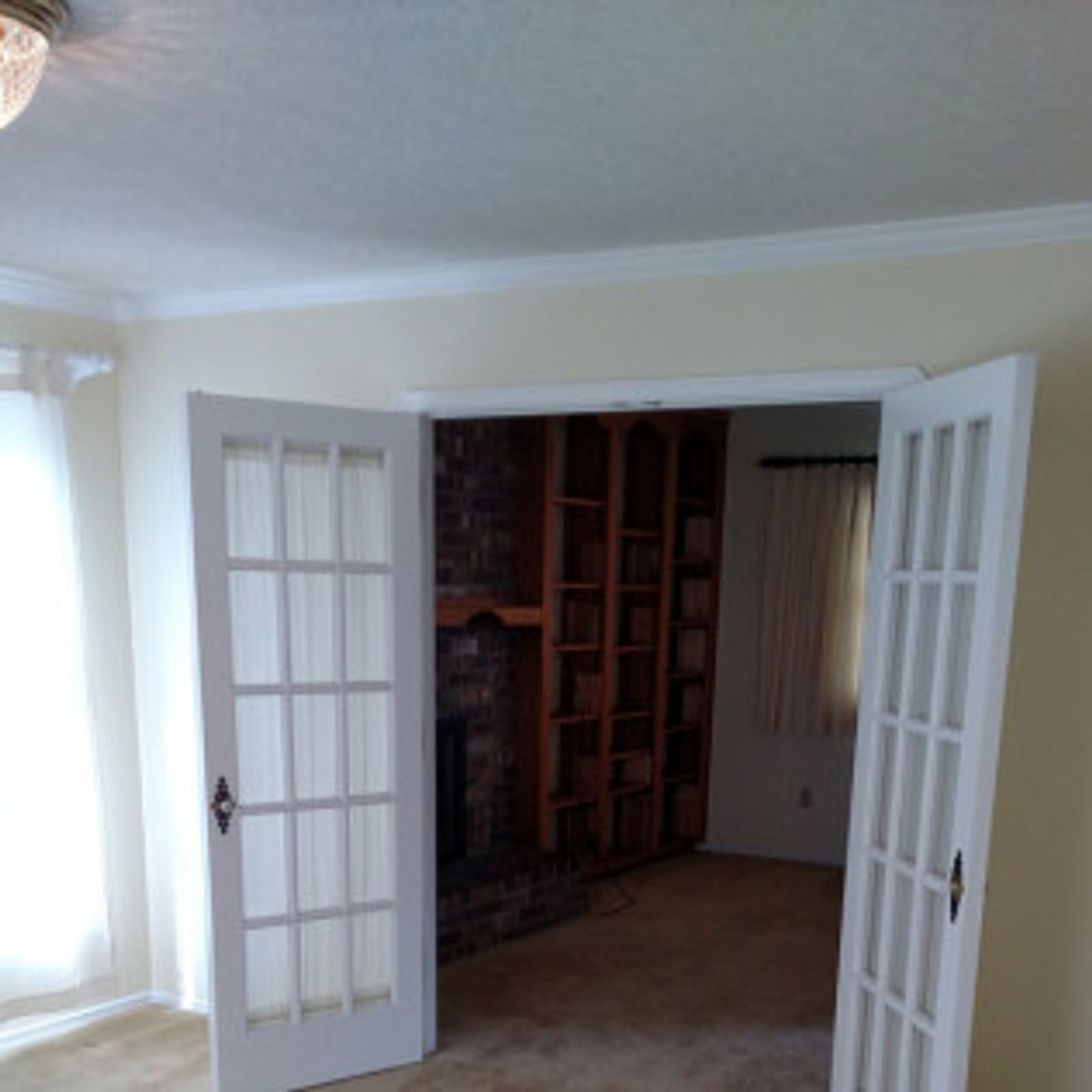 French doors open into a room with a brick fireplace and built-in bookshelves.