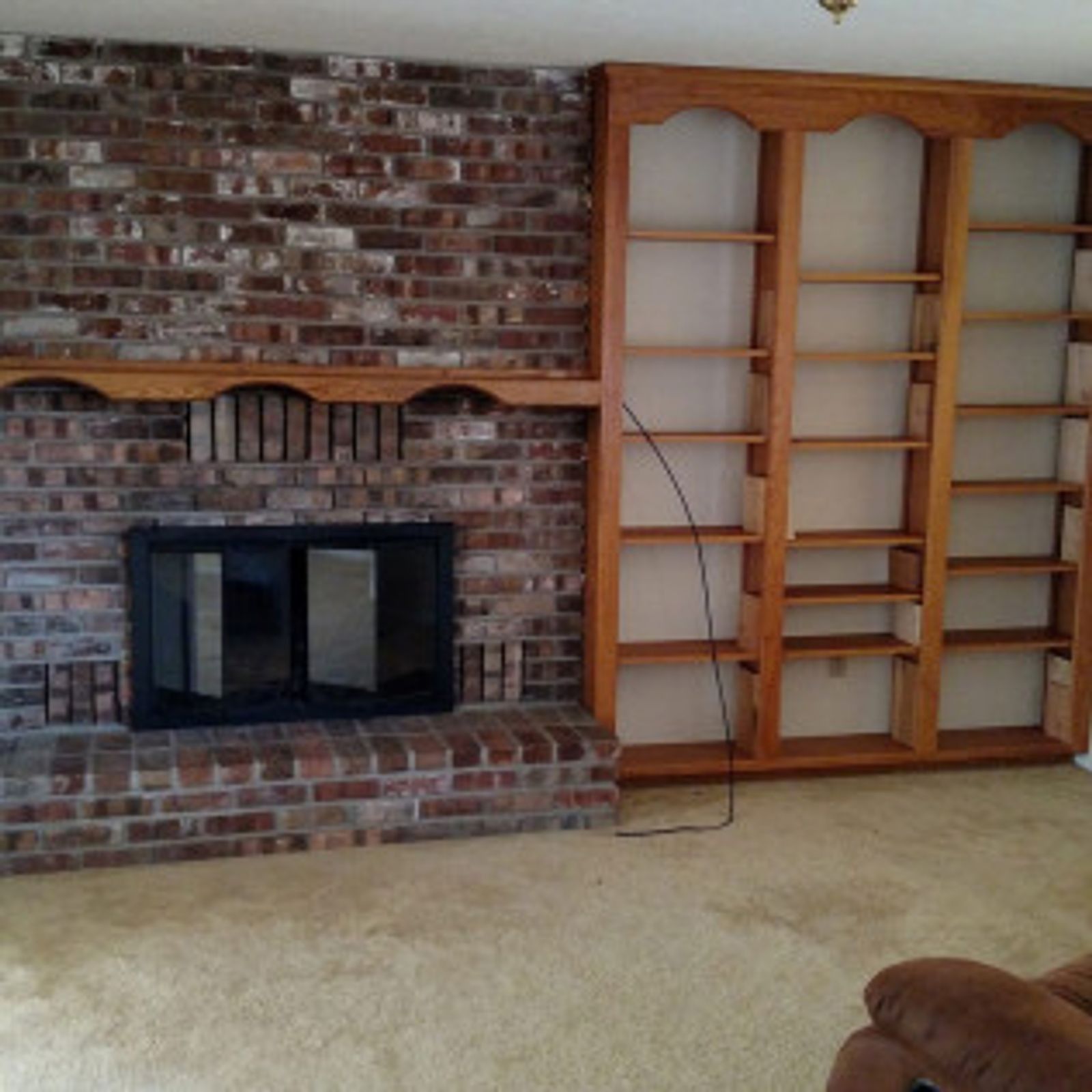 Brick fireplace with built-in wooden bookshelves; tan carpet and neutral wall.