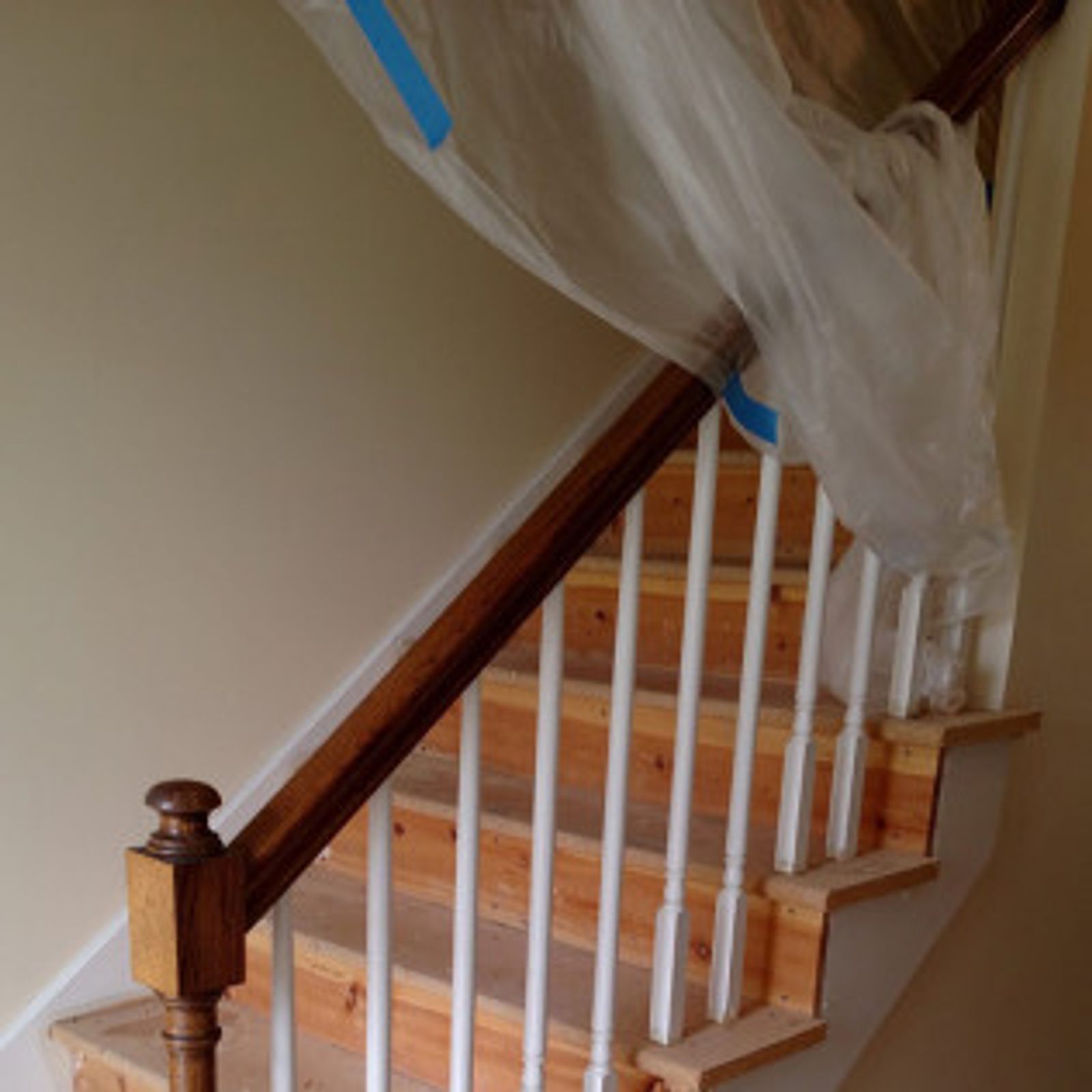 Wooden staircase with white balusters, brown handrail, and plastic sheeting for protection.