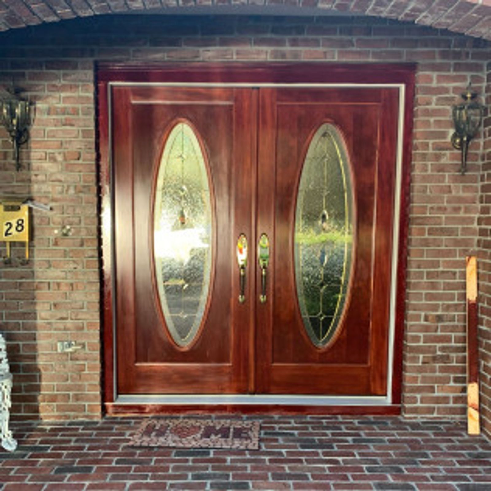 Double wooden front doors with oval glass panels, set in a brick facade, lit by wall sconces.