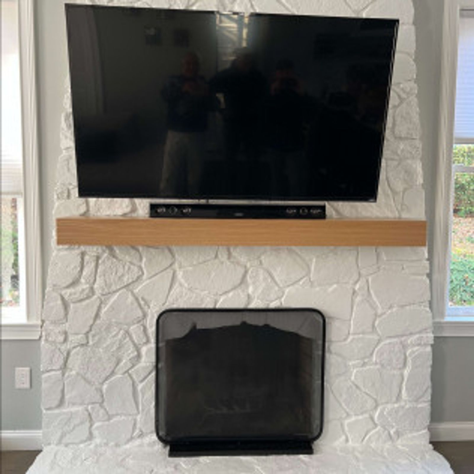 Large TV mounted above a light wood mantel on a white stone fireplace with a black fire screen.