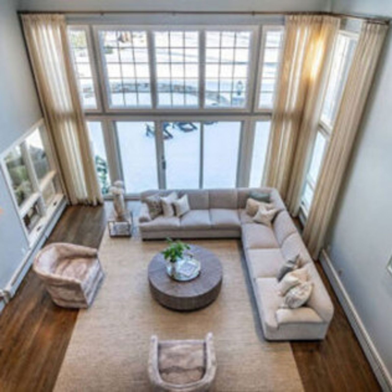Spacious living room with large windows, neutral sectional sofa, round coffee table, and two armchairs on a beige rug.