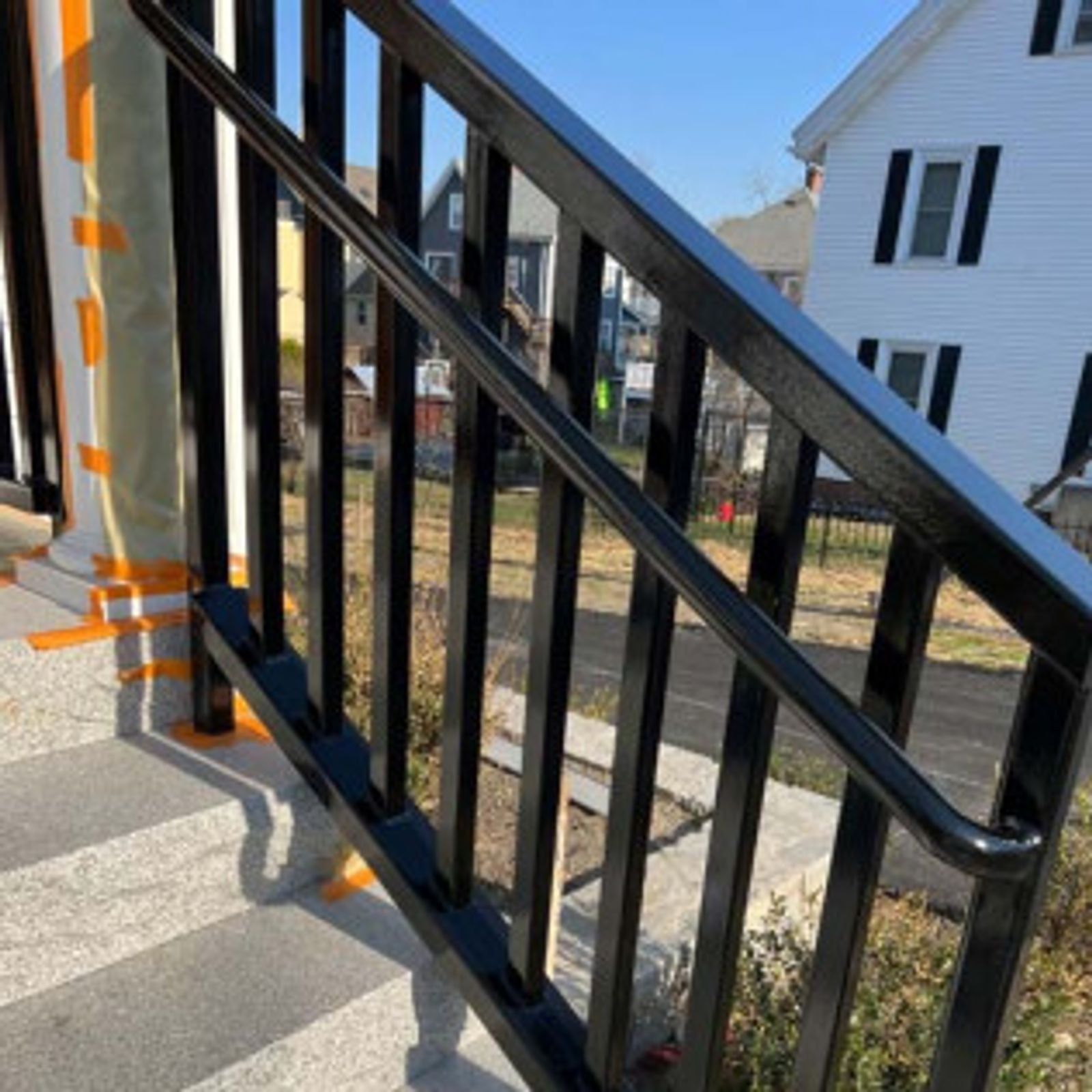 Black metal handrail on outdoor steps with a residential backdrop.