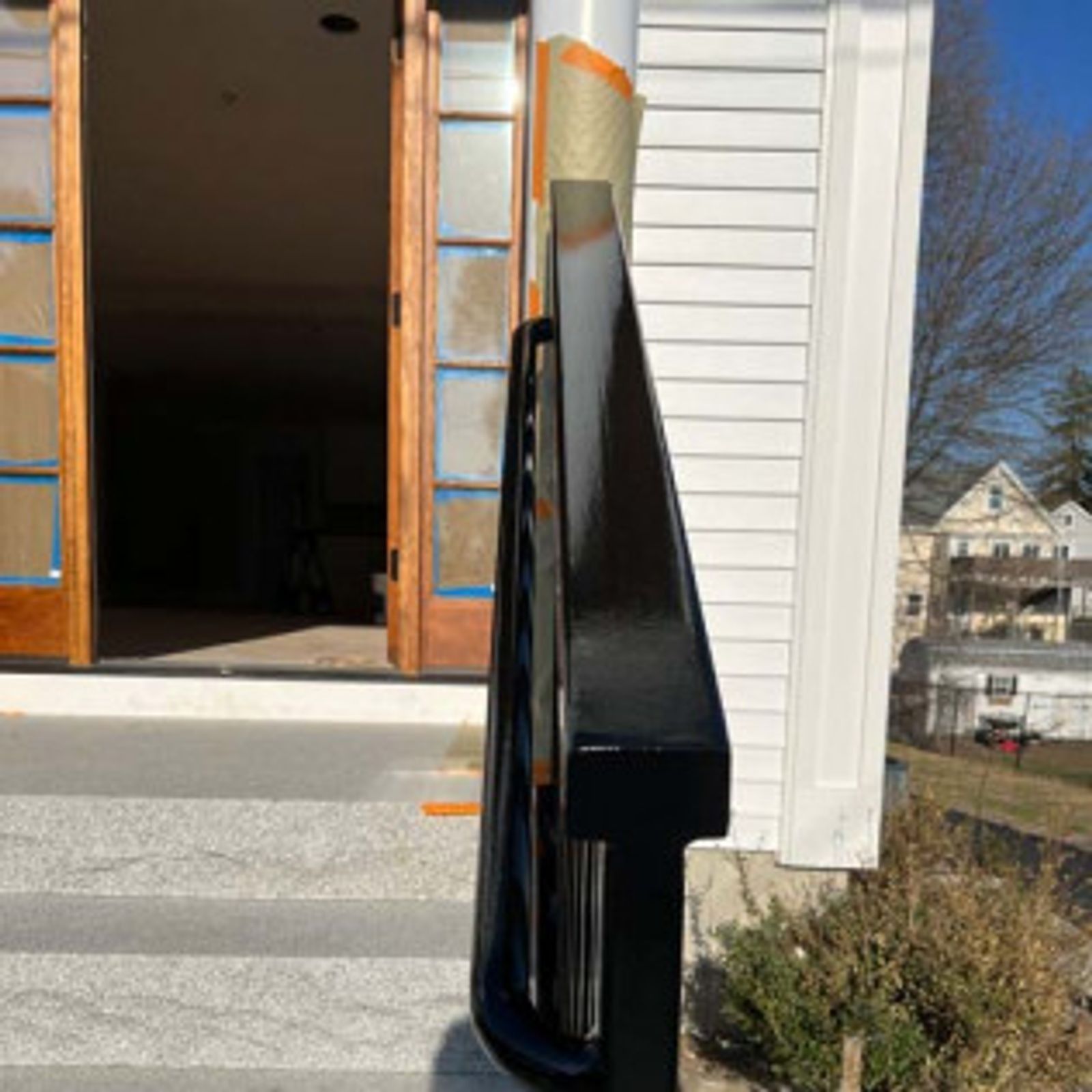 Black handrail on gray steps leading to a building with open wooden doors. White siding to the right.