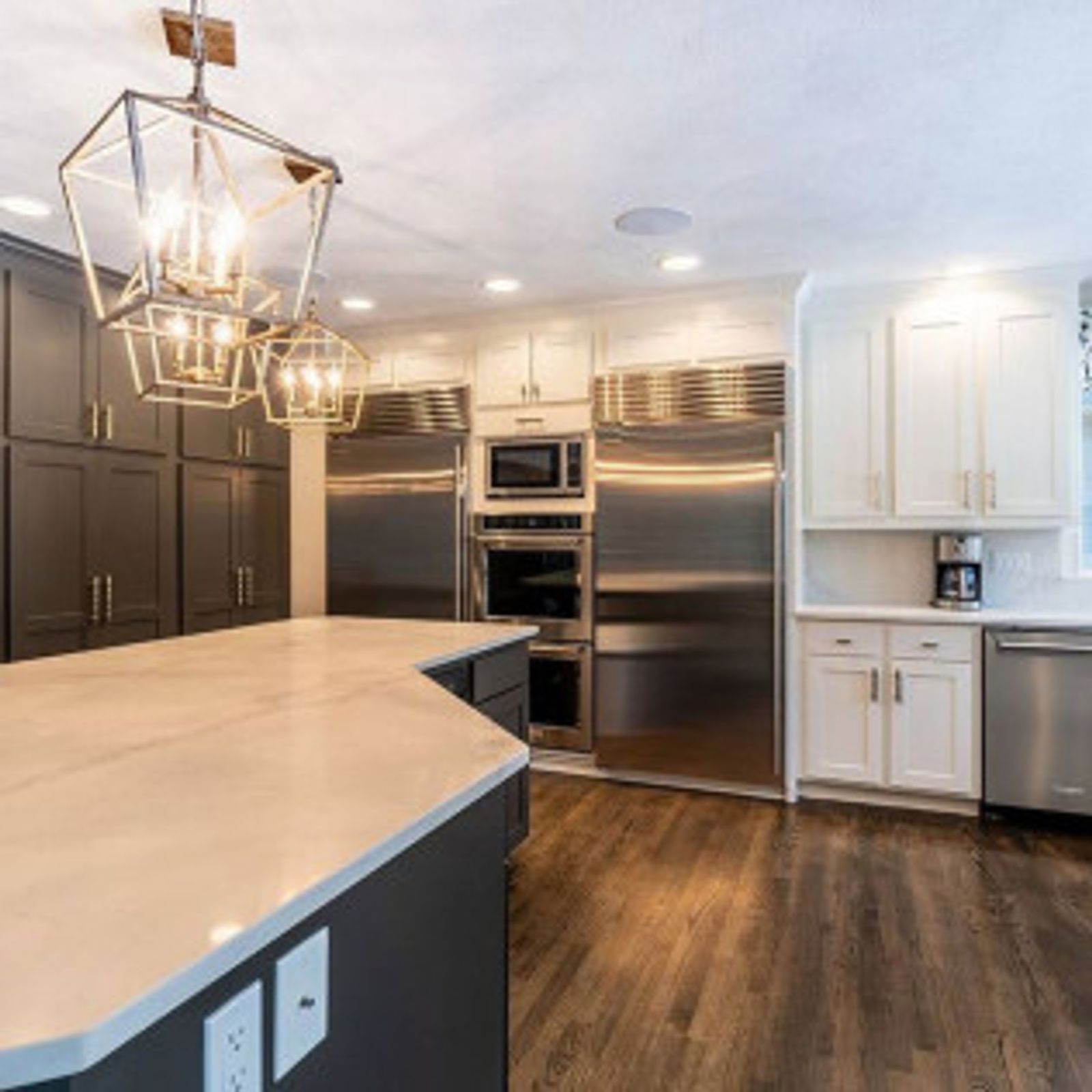 Modern kitchen with gray and white cabinets, stainless steel appliances, and a marble-topped island.