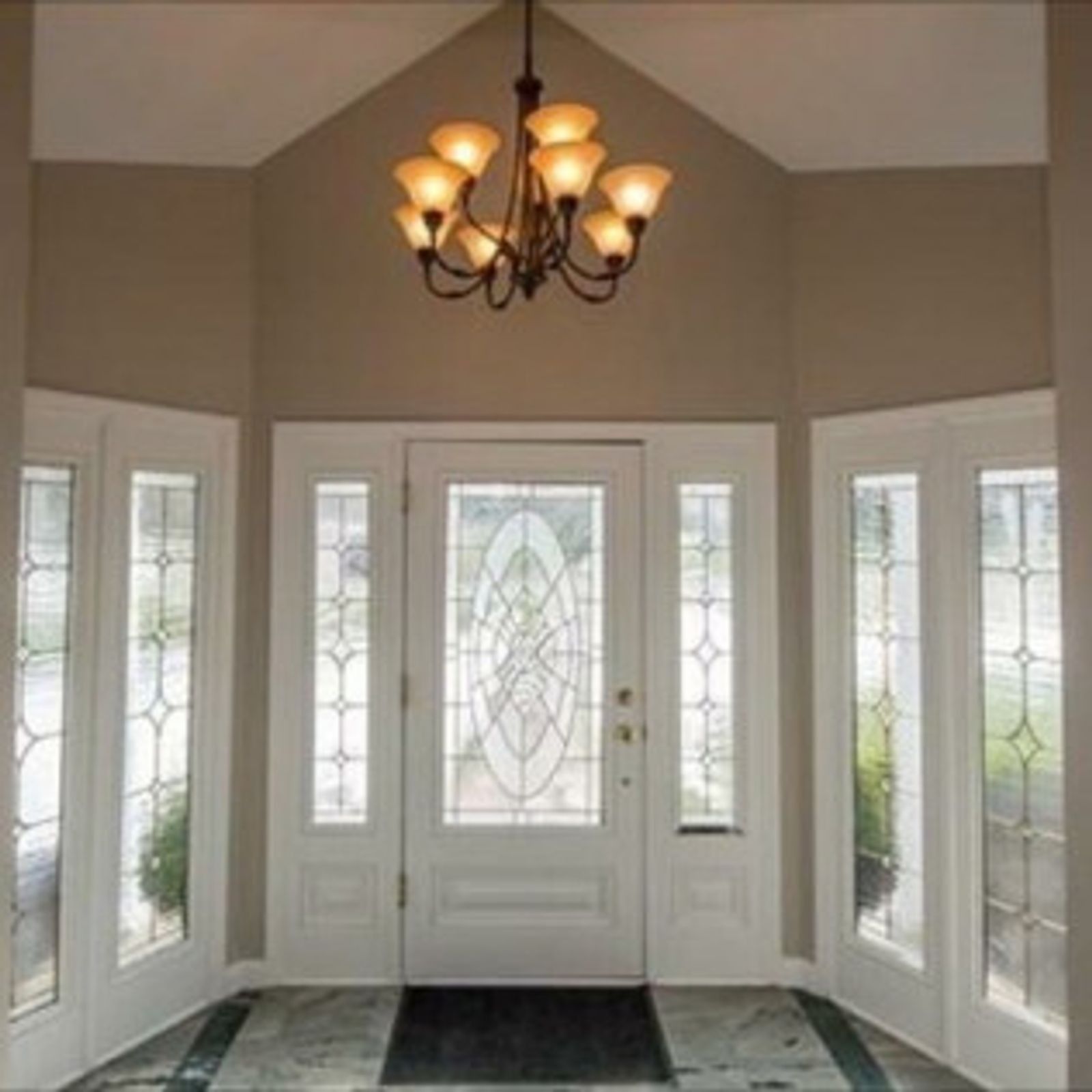 A grand entryway with a white door, stained glass, and a chandelier. Beige walls with a checkered floor.