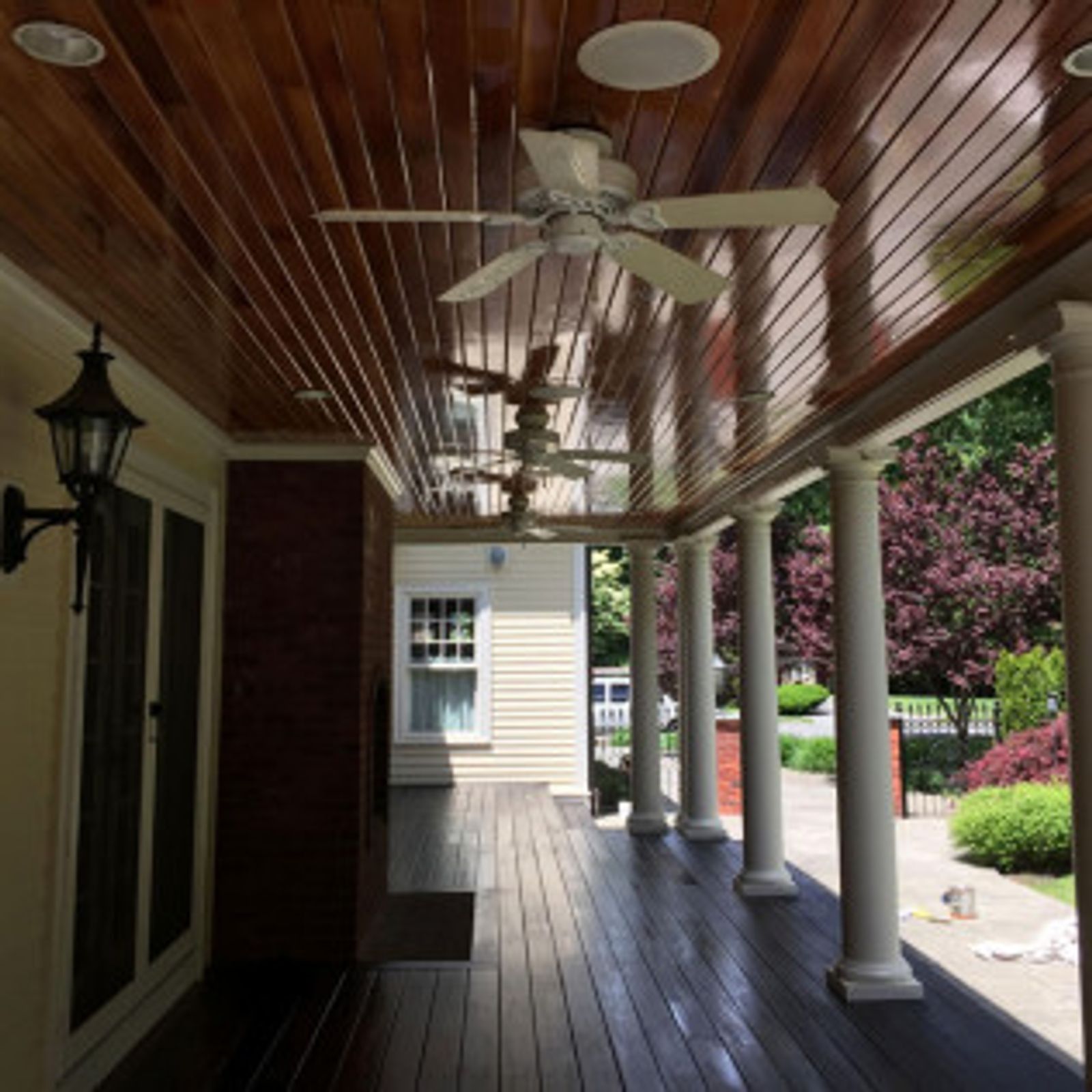 Covered porch with wood ceiling and floor, white columns, two ceiling fans, and a street view.