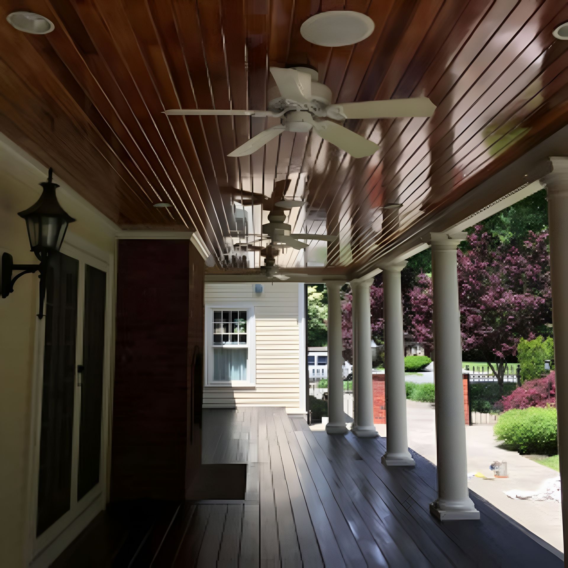 Covered porch with wood ceiling and floor, white columns, two ceiling fans, and an outdoor light.