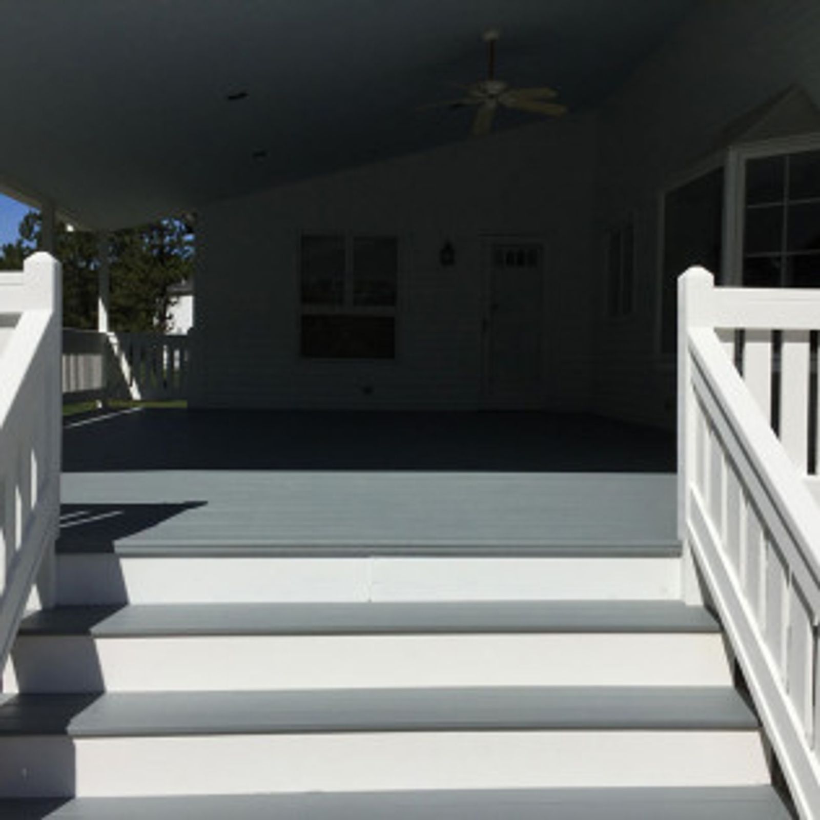 White deck steps leading to a covered porch with gray flooring, white walls, and a ceiling fan.