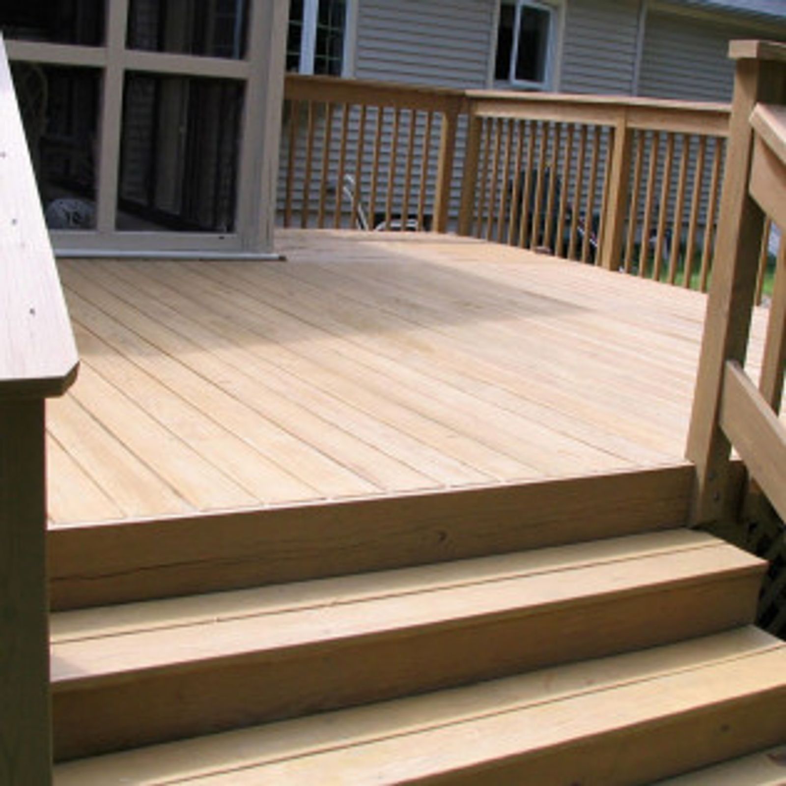 Wooden deck with three steps leading down, attached to a house with a sliding glass door.