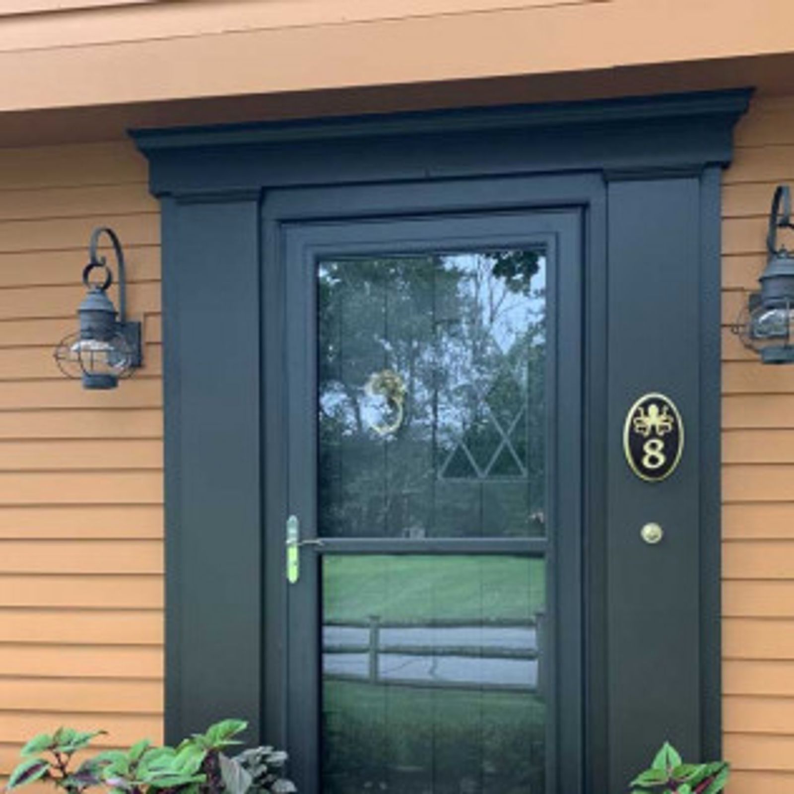Black framed door with a screen, flanked by sconces, address plaque with an 8.