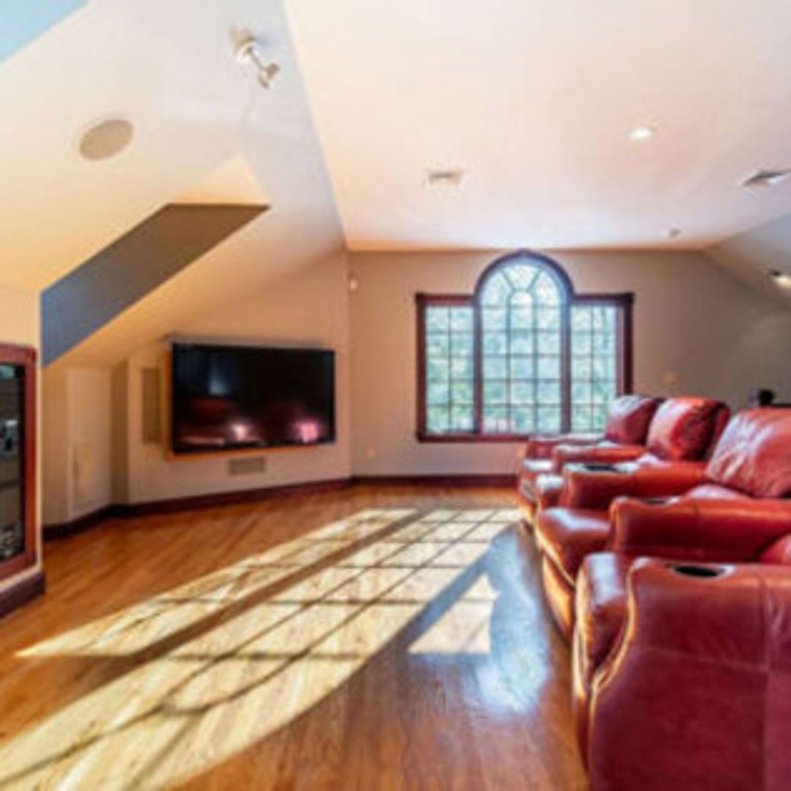 Home theater with red leather recliners, large TV, hardwood floor, and arched window letting in light.