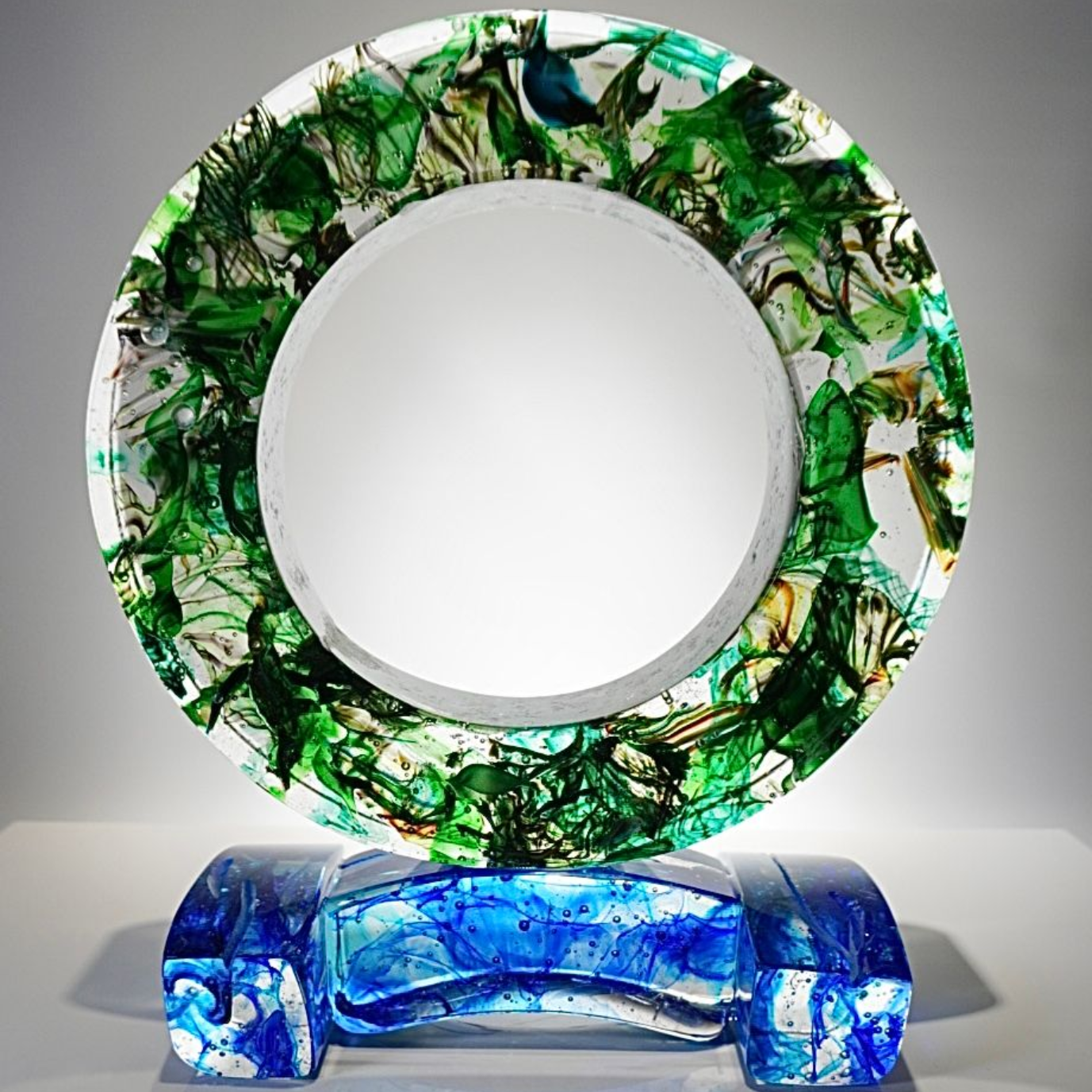 A green glass sculpture is sitting on top of a blue base on a table.