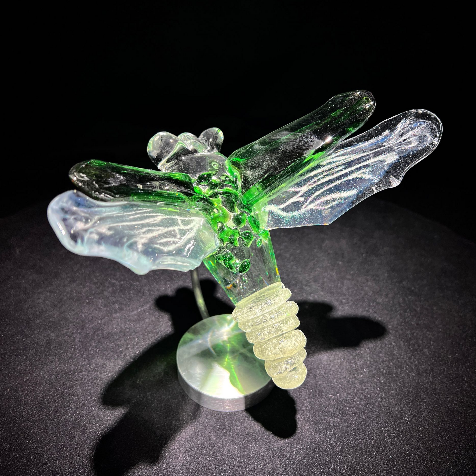 A glass firefly sitting on a black surface.