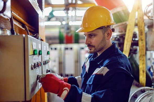 A man in a hard hat is working on a machine in a factory.