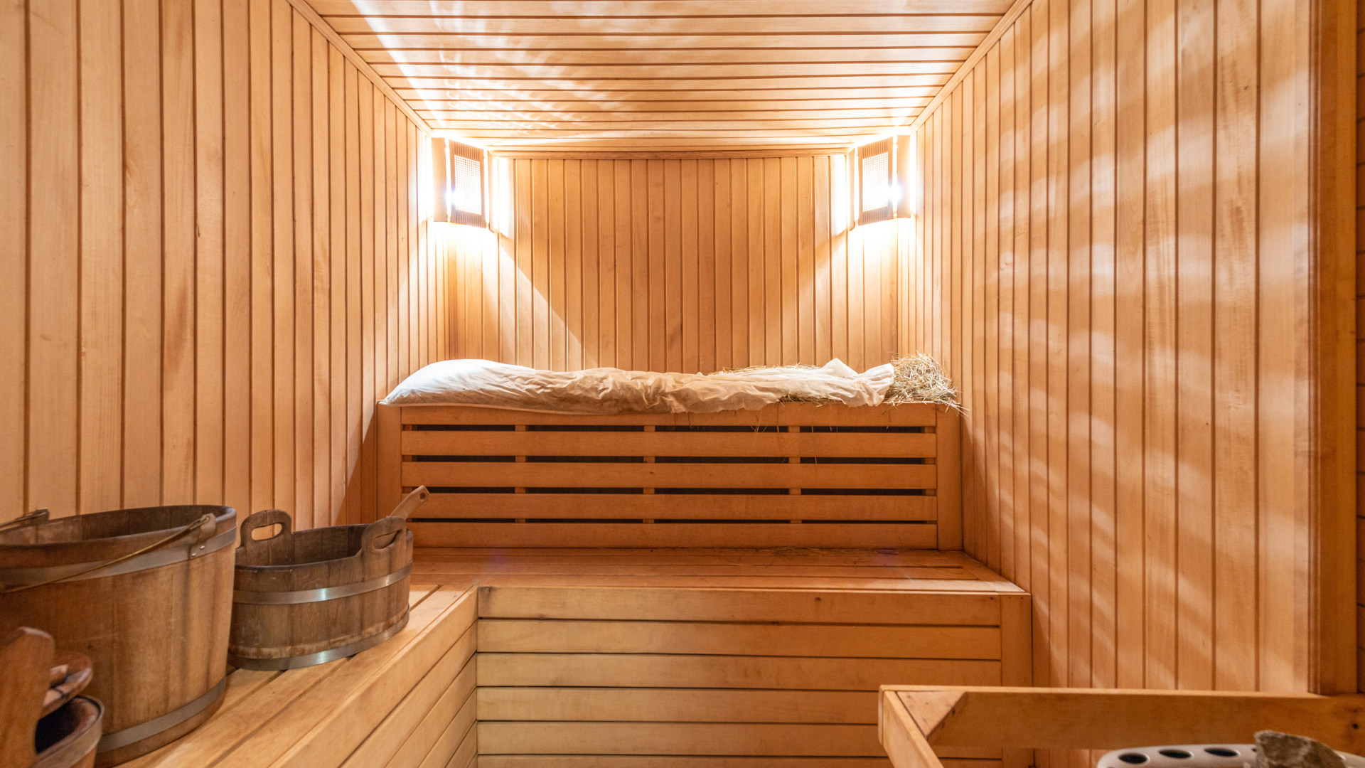 A wooden sauna with a bed and buckets in it.