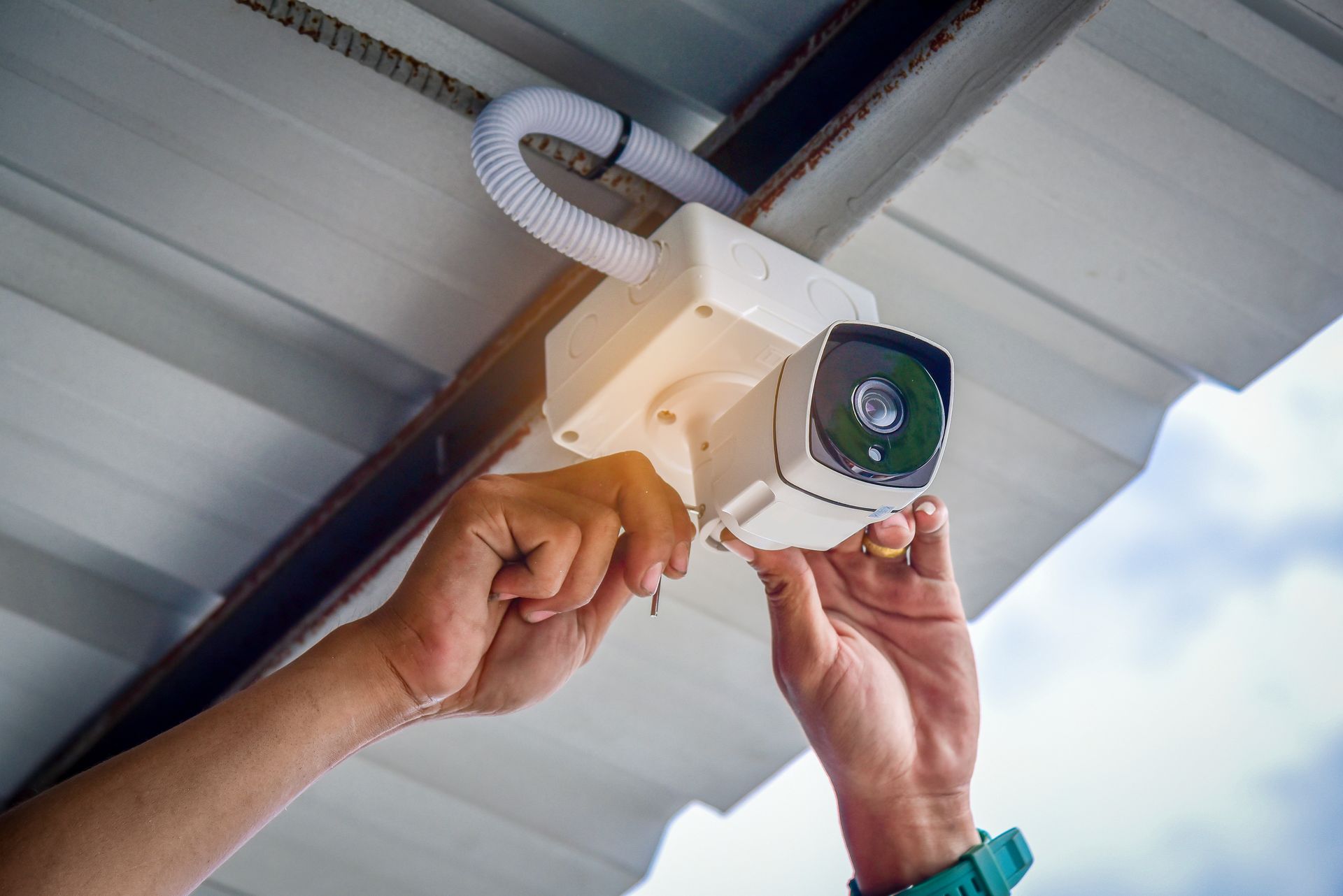 A technician installing an outdoor security camera under the eaves of a home.