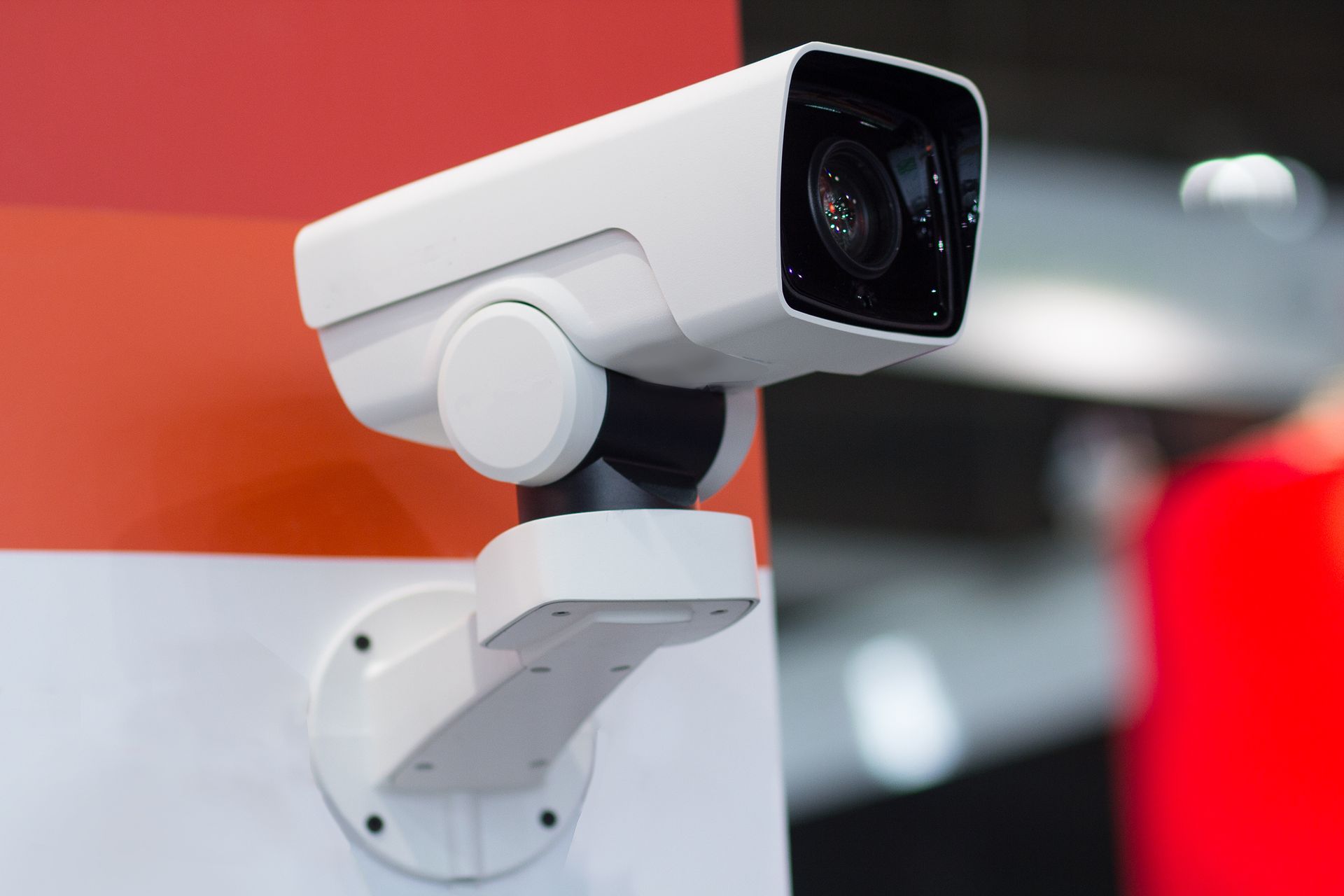 Modern security camera mounted on an indoor wall near a ceiling light fixture.