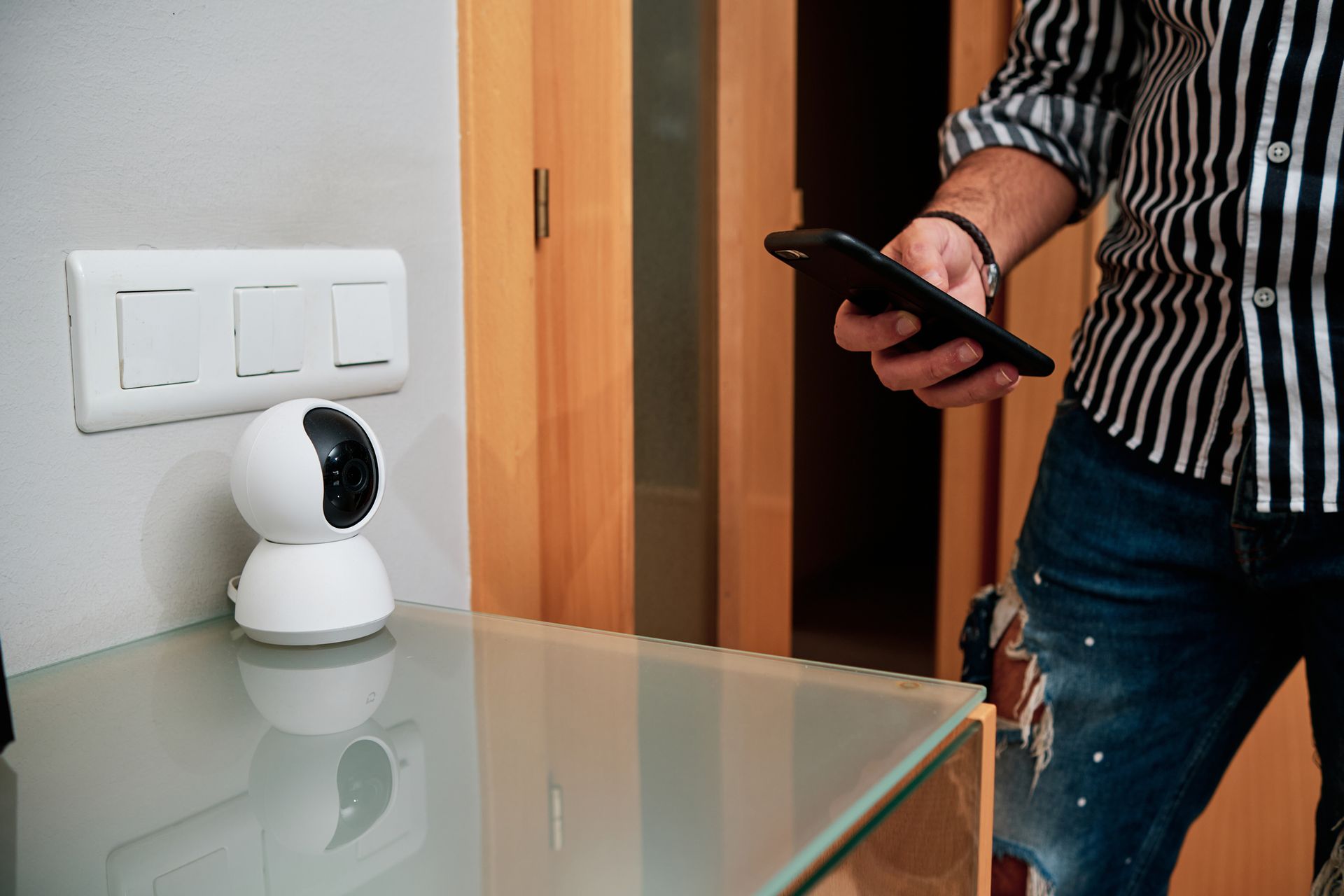 A man stands next to a security camera with a smartphone in hand.
