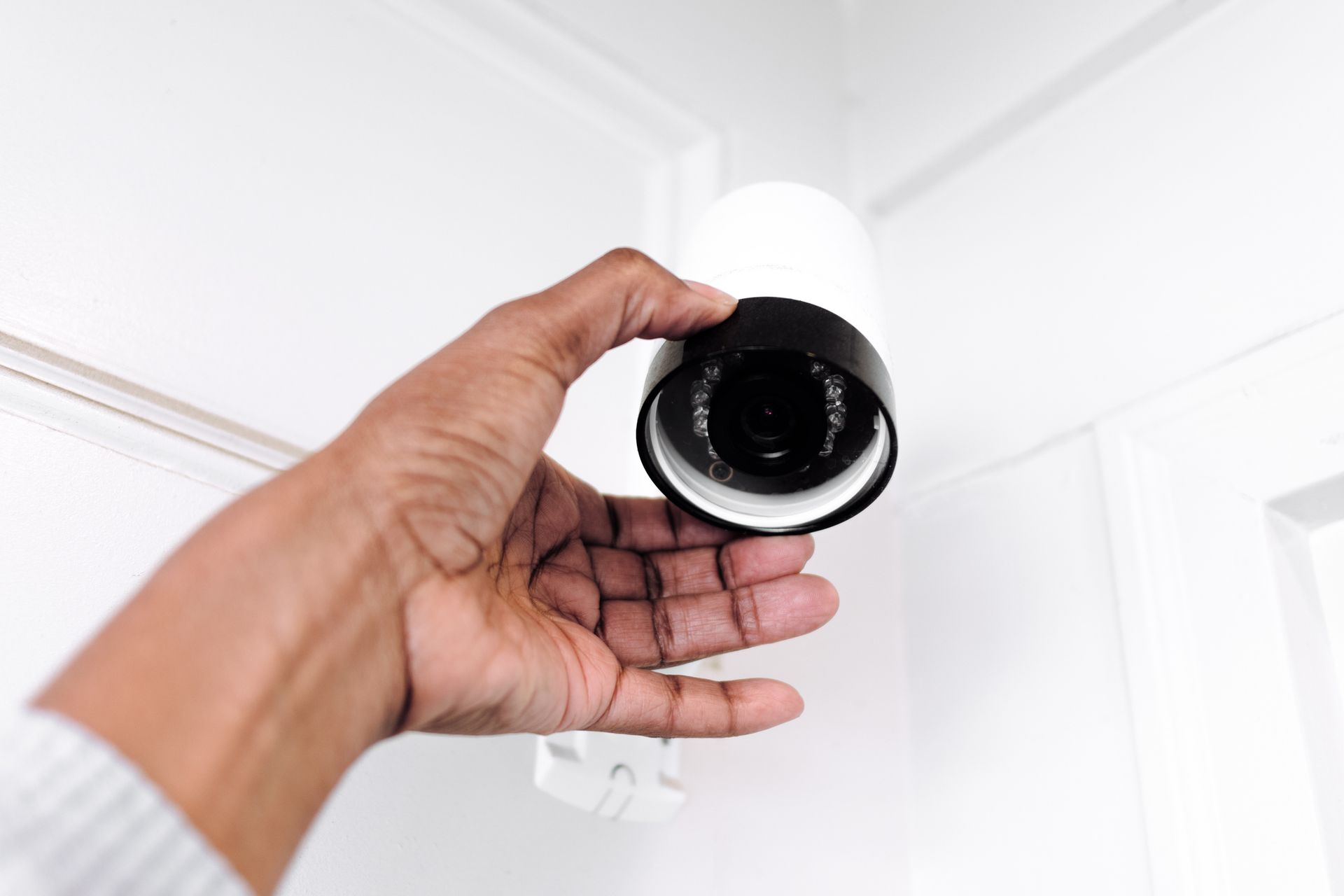 Close-up of a hand adjusting a security camera placed in the corner of a ceiling.