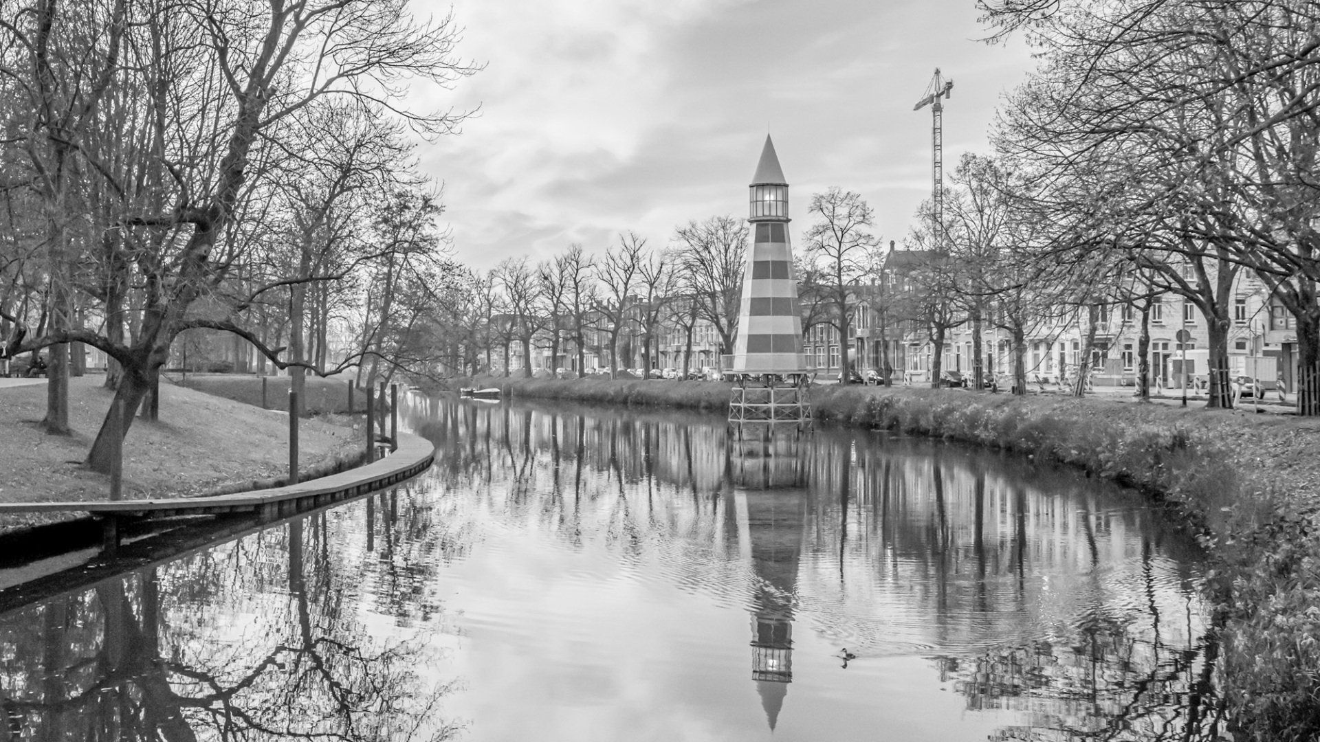 Een gestreepte vuurtoren staat midden in een rustig kanaal, geflankeerd door kale bomen en weerspiegeld in het stille water.