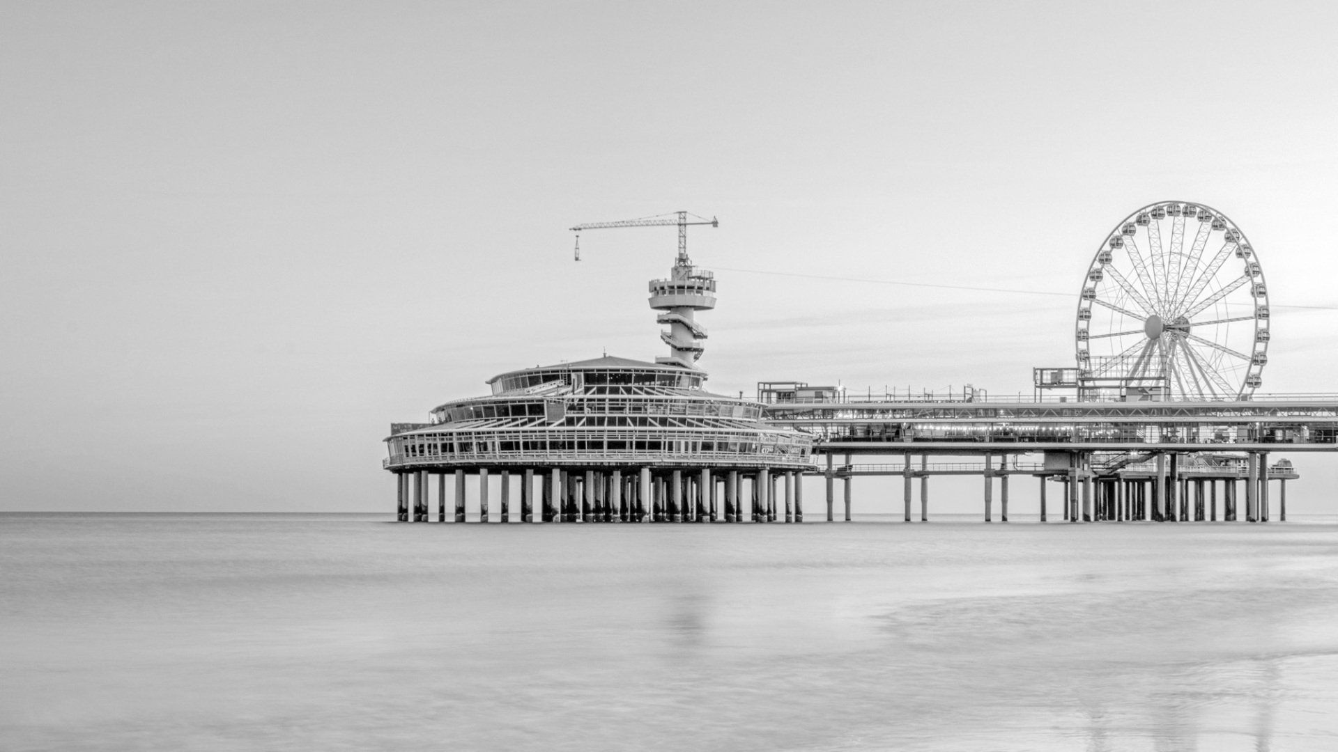 Een zwart-witfoto van de Scheveningenpier in Nederland, met een hoge uitkijktoren en een reuzenrad.
