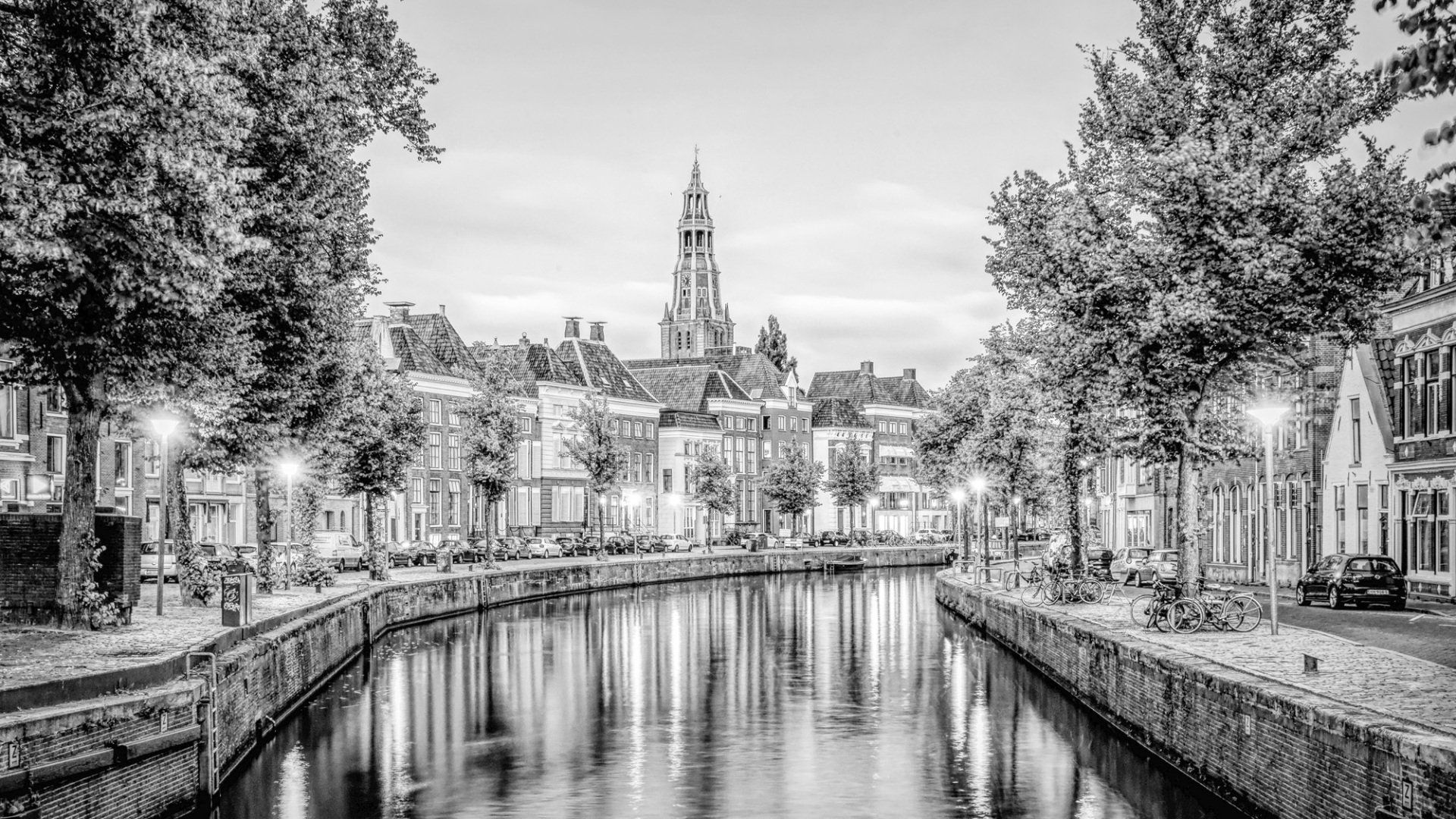 Zwart-witfoto van een Nederlands kanaal met bomen en historische gebouwen, met in het midden een hoge kerktoren.