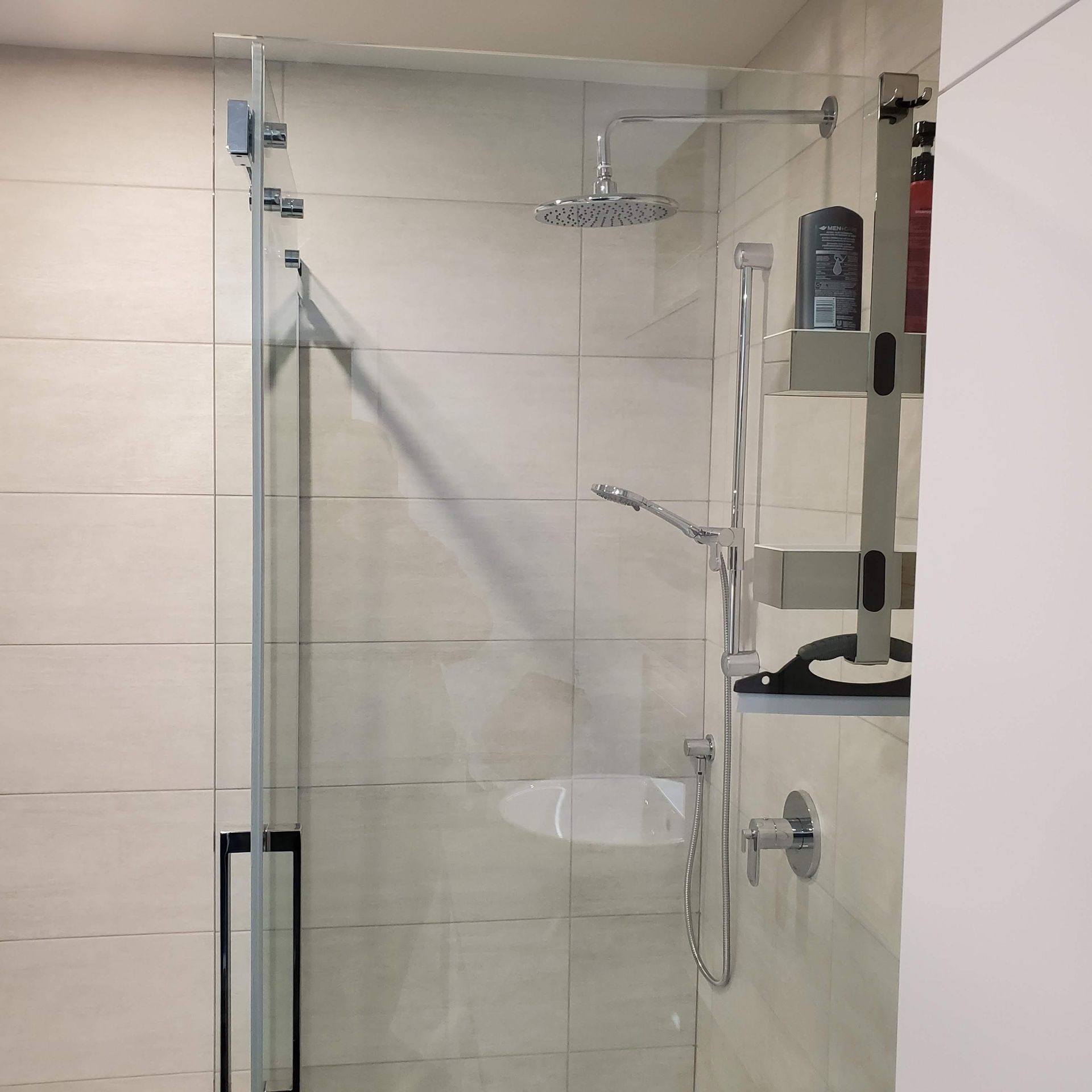 Une salle de bain avec une douche et une bouteille de shampoing sur une étagère