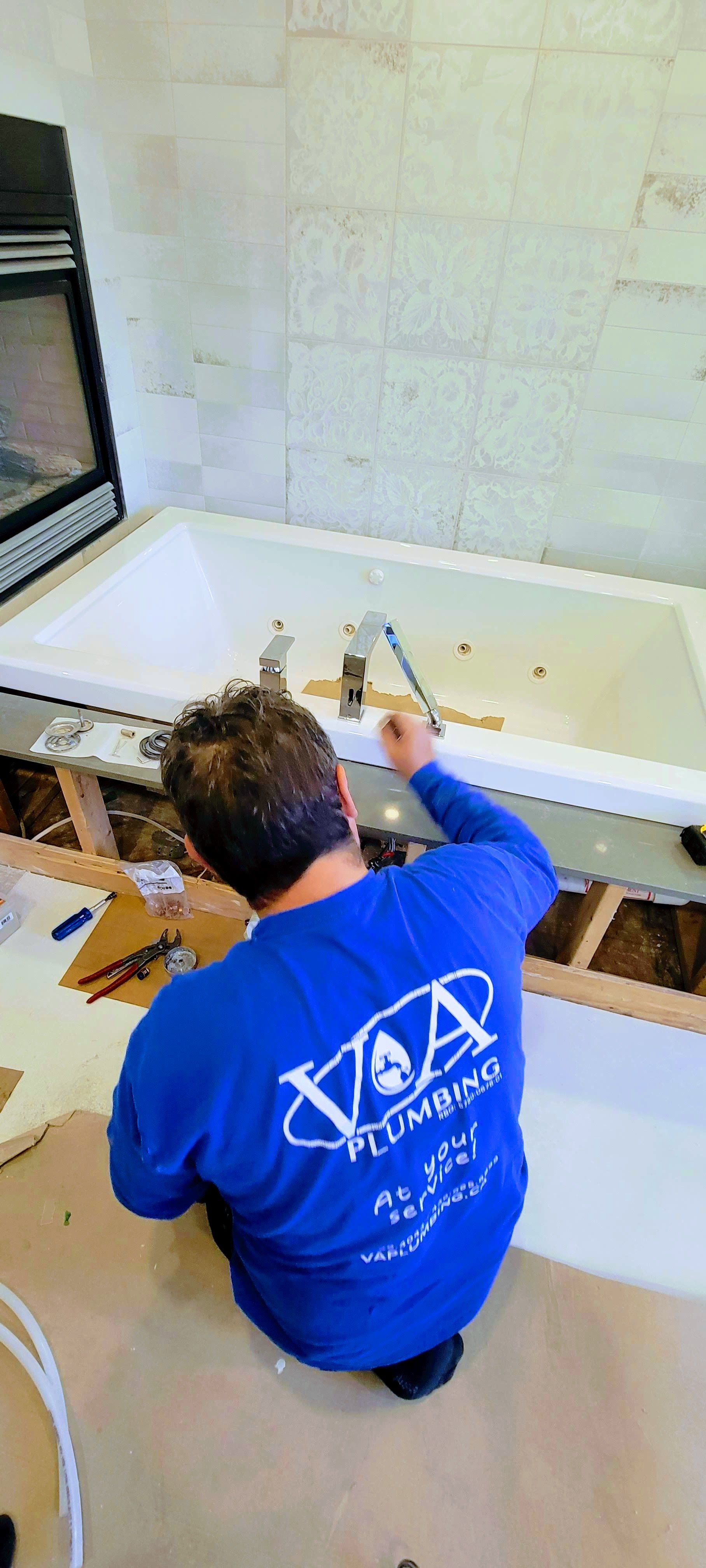 Un homme en chemise bleue est à genoux devant une baignoire.