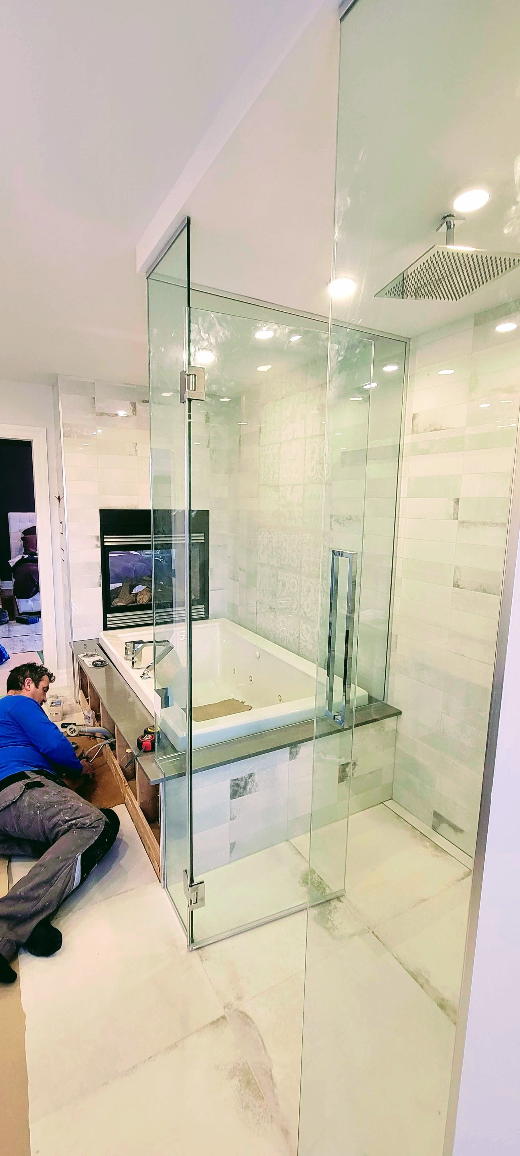 Un homme installe une porte de douche en verre dans une salle de bain.