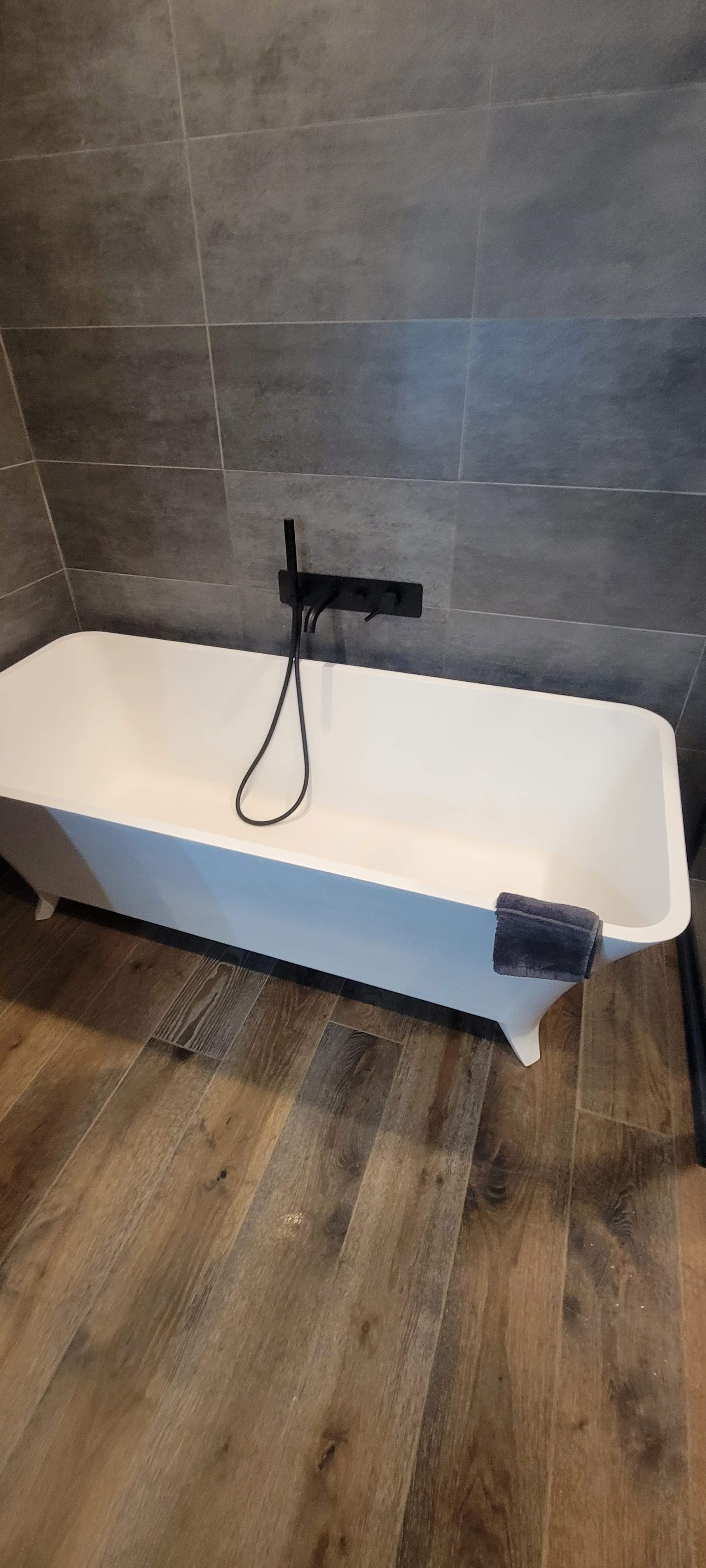 Une baignoire blanche est posée sur un plancher en bois dans une salle de bain.