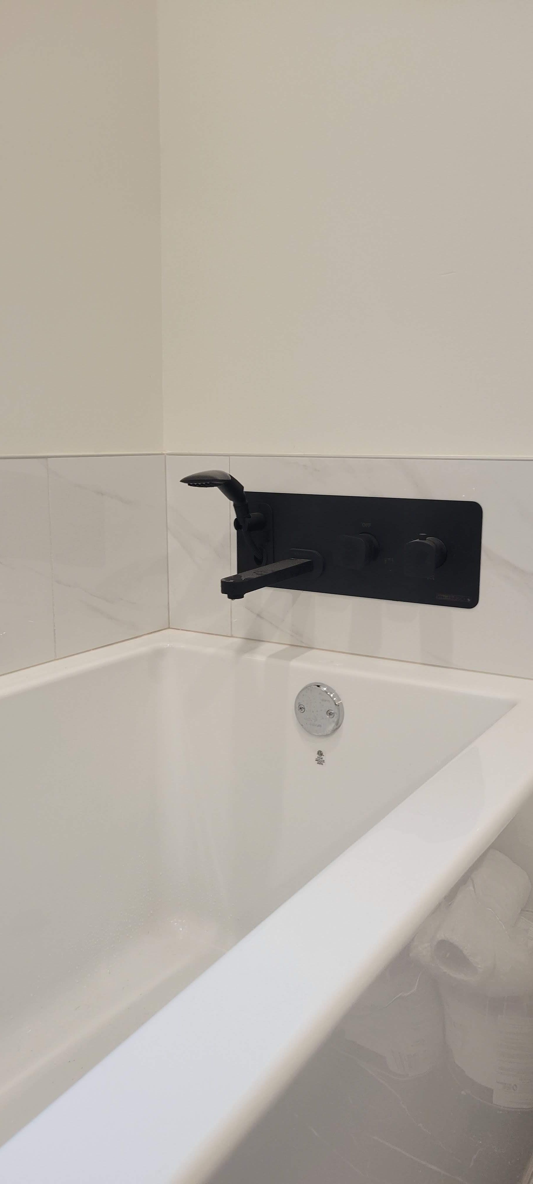 Une baignoire avec un robinet noir sur le mur à côté.